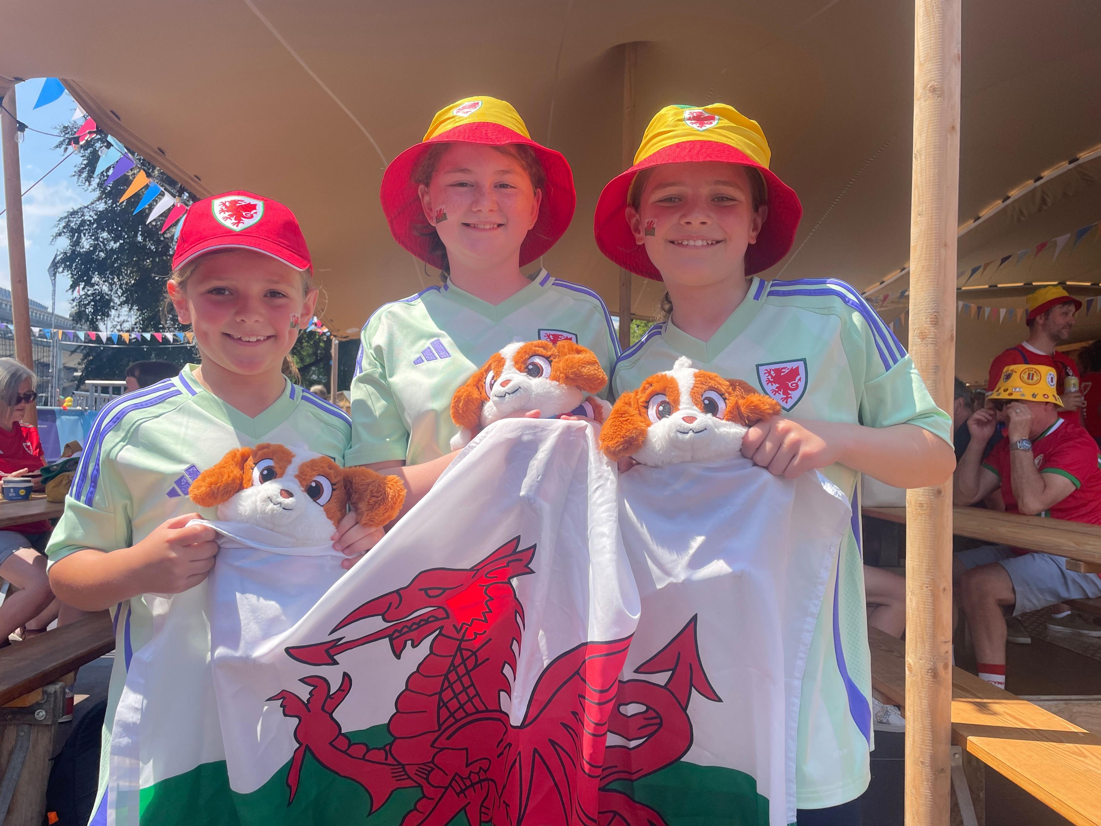 Three girls, holding a Wales fan and wearing Wales bucket hats