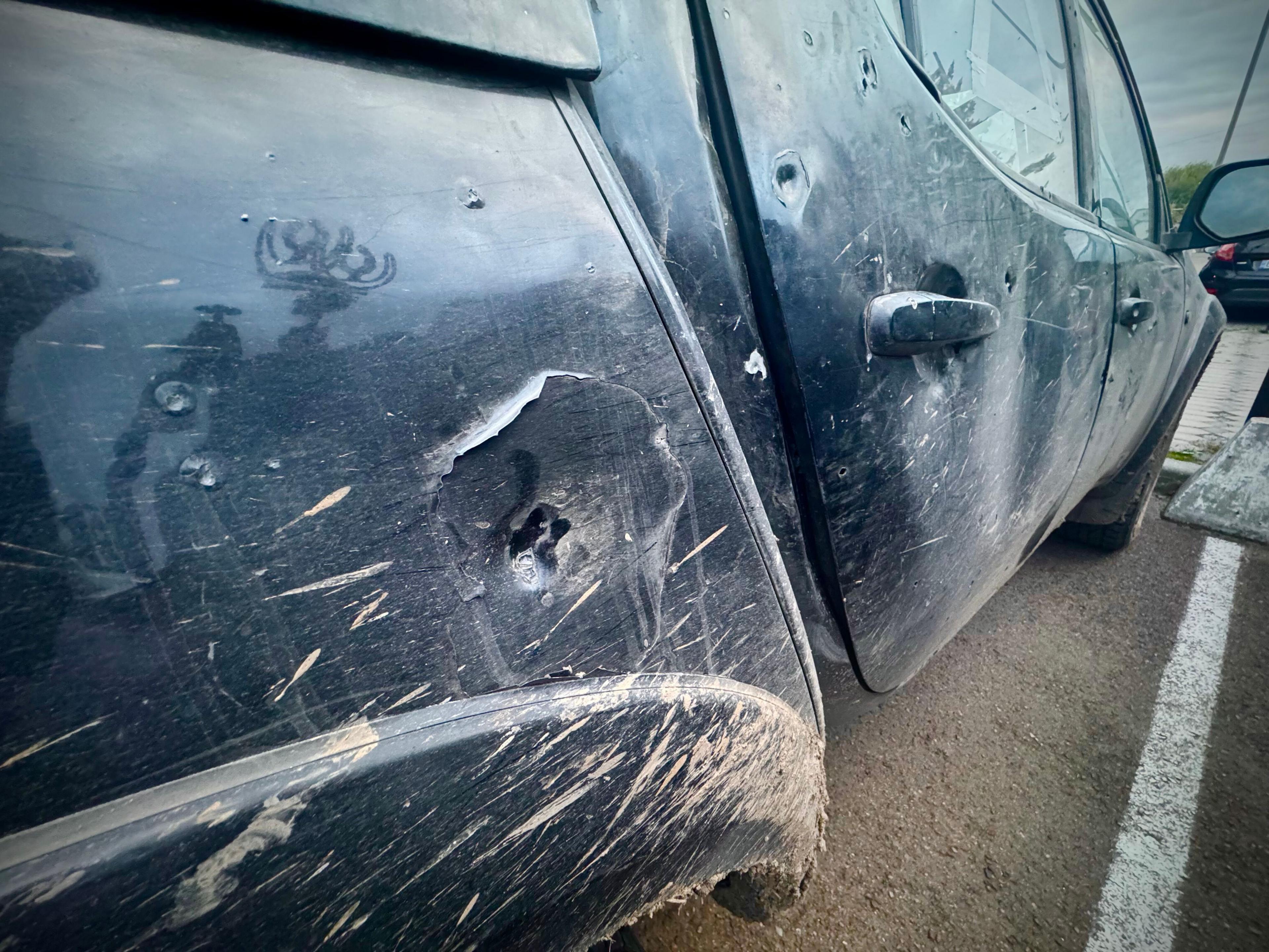 A close-up of the side of the black Mitsubishi pickup truck shows mud splashes and dents, with what looks like bullet holes all along the middle of the car from door handle to door handle.