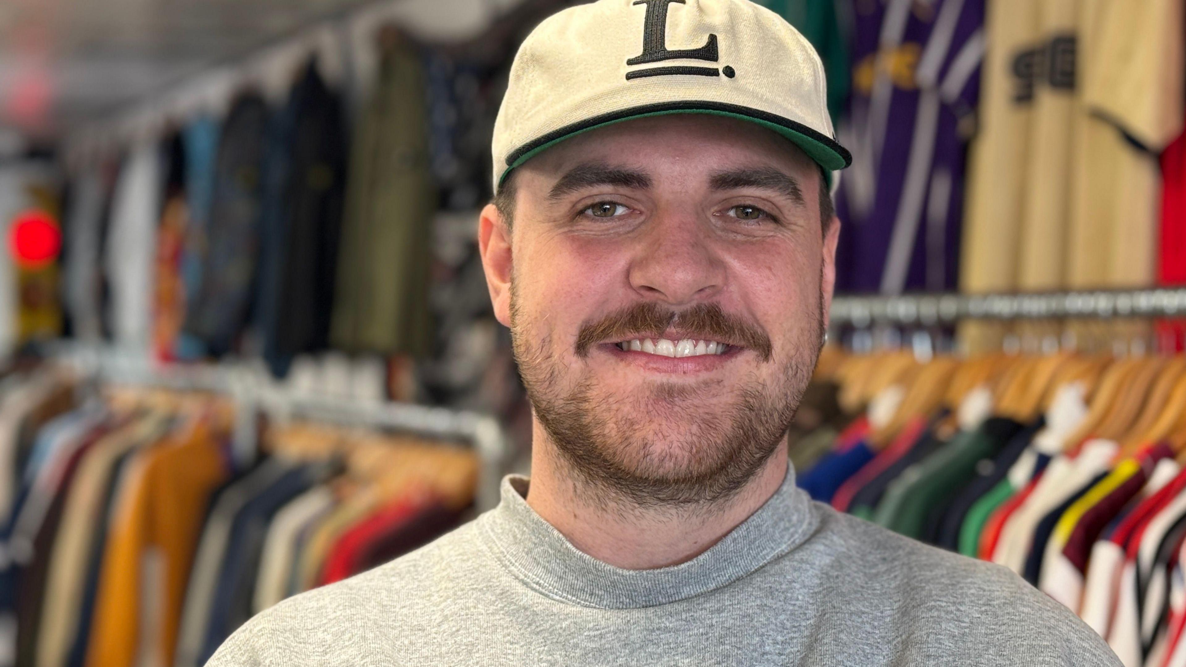 Daniel Evans, with short brown hair and beard, wearing white T shirt in his shop