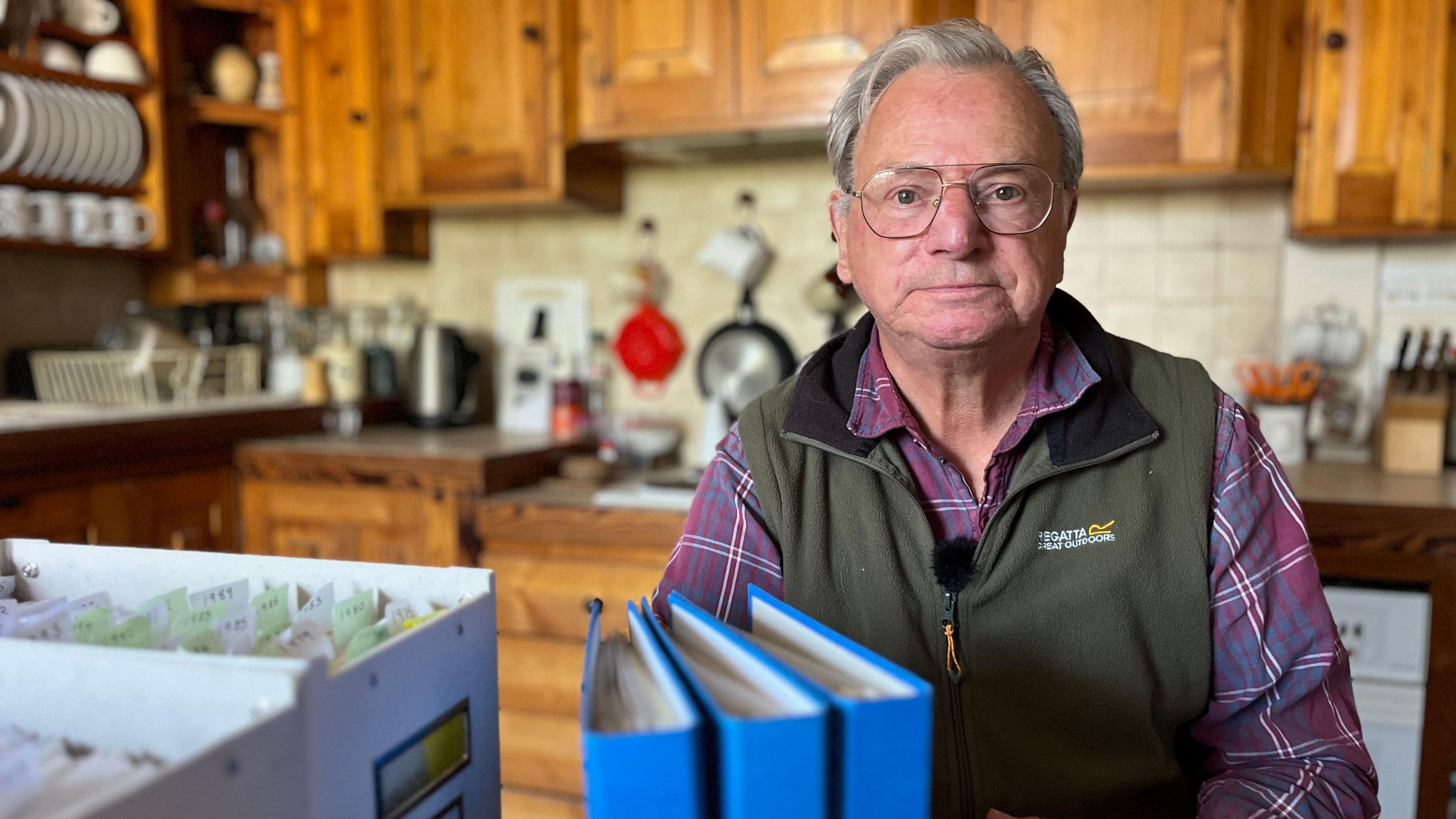 Man sits at his kitchen table with boxes and files full of past newspaper editions 