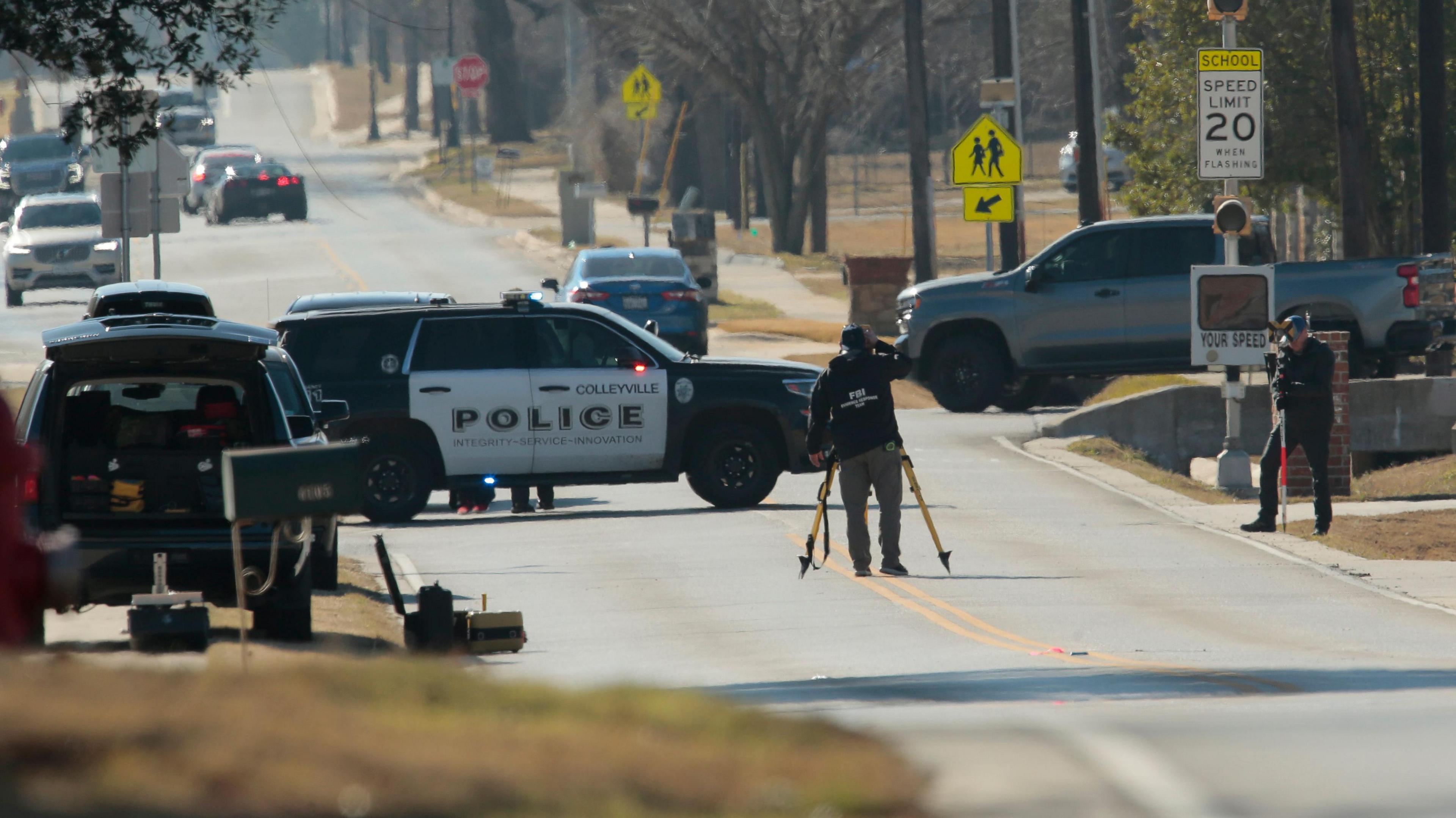 Police continue their investigation on a road near the synagogue, surrounded by police vehicles