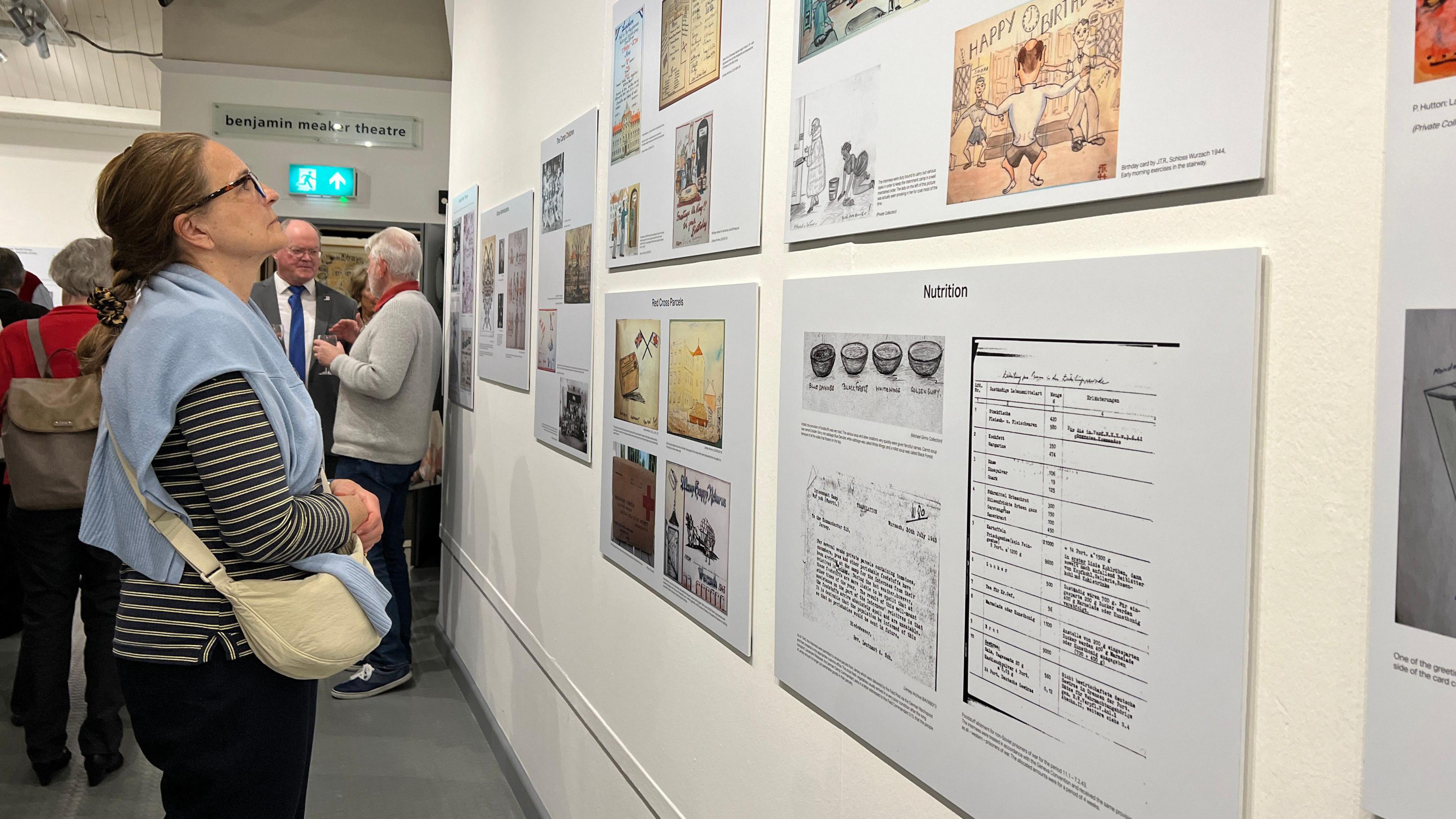 A woman looks at some of the artwork while some people enjoy some glasses of wine in the background