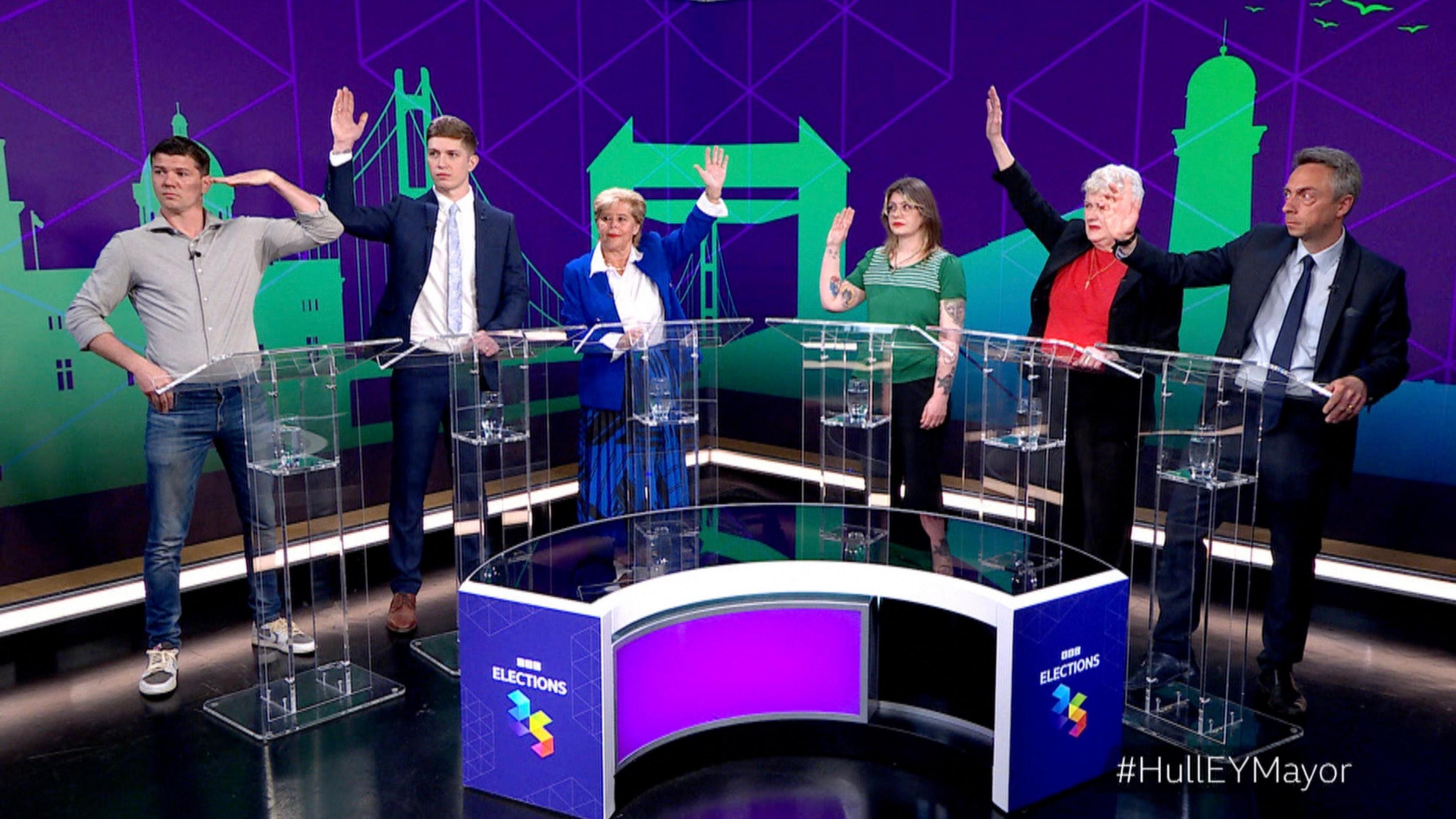 Luke Campbell and the five defeated mayoral candidates taking part in a BBC debate in a TV studio. The candidates stand in a semi-circle. All have their hands raised, except Campbell whose hand is half-raised.