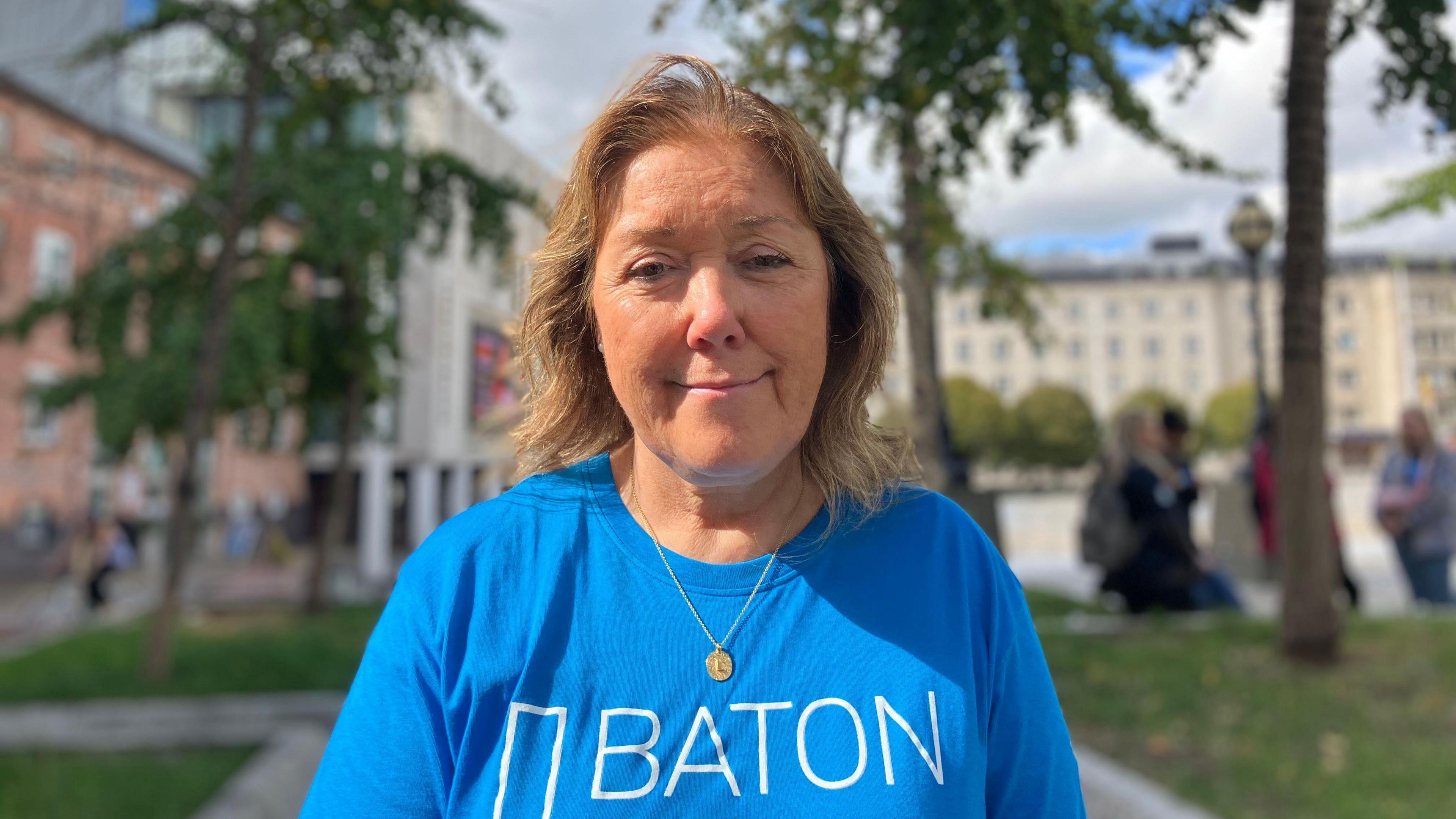 Kate Cleal, who has mid-length brown hair. She is wearing a blue baton of hope t-shirt.