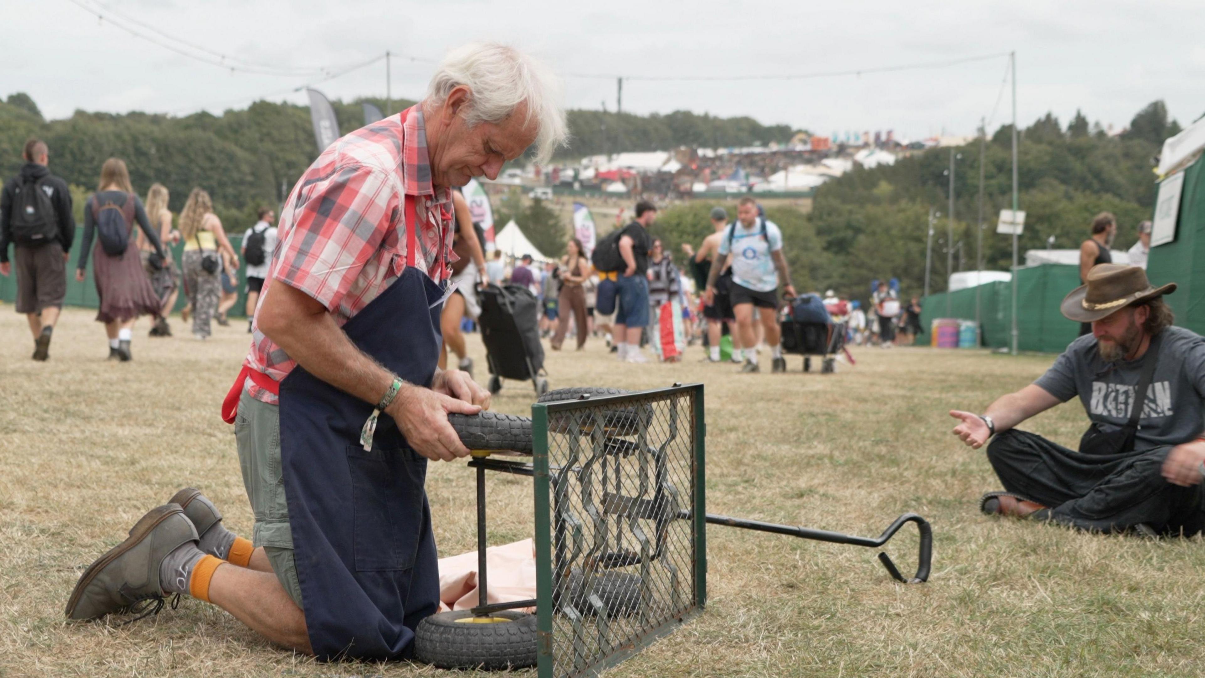 Charles Cole fixing a trolley at the festival. He is on his knees, stuffing the wheel with fabric.