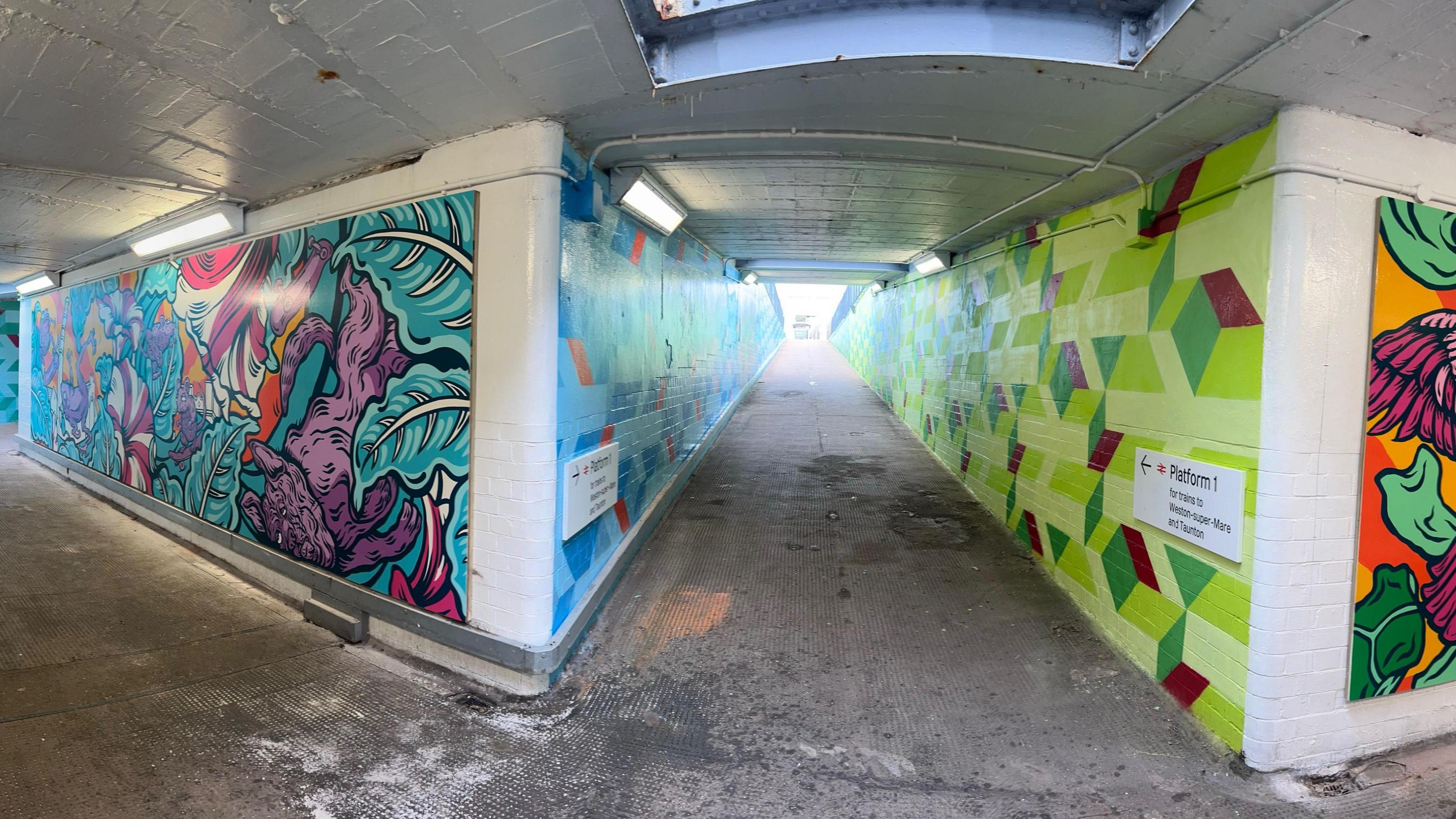 Image shows the Bedminster station underpass from a different angle, with a path leading to platform one. The path stretching up to the platform has one green and one blue wall, with varying shades and patterns. 