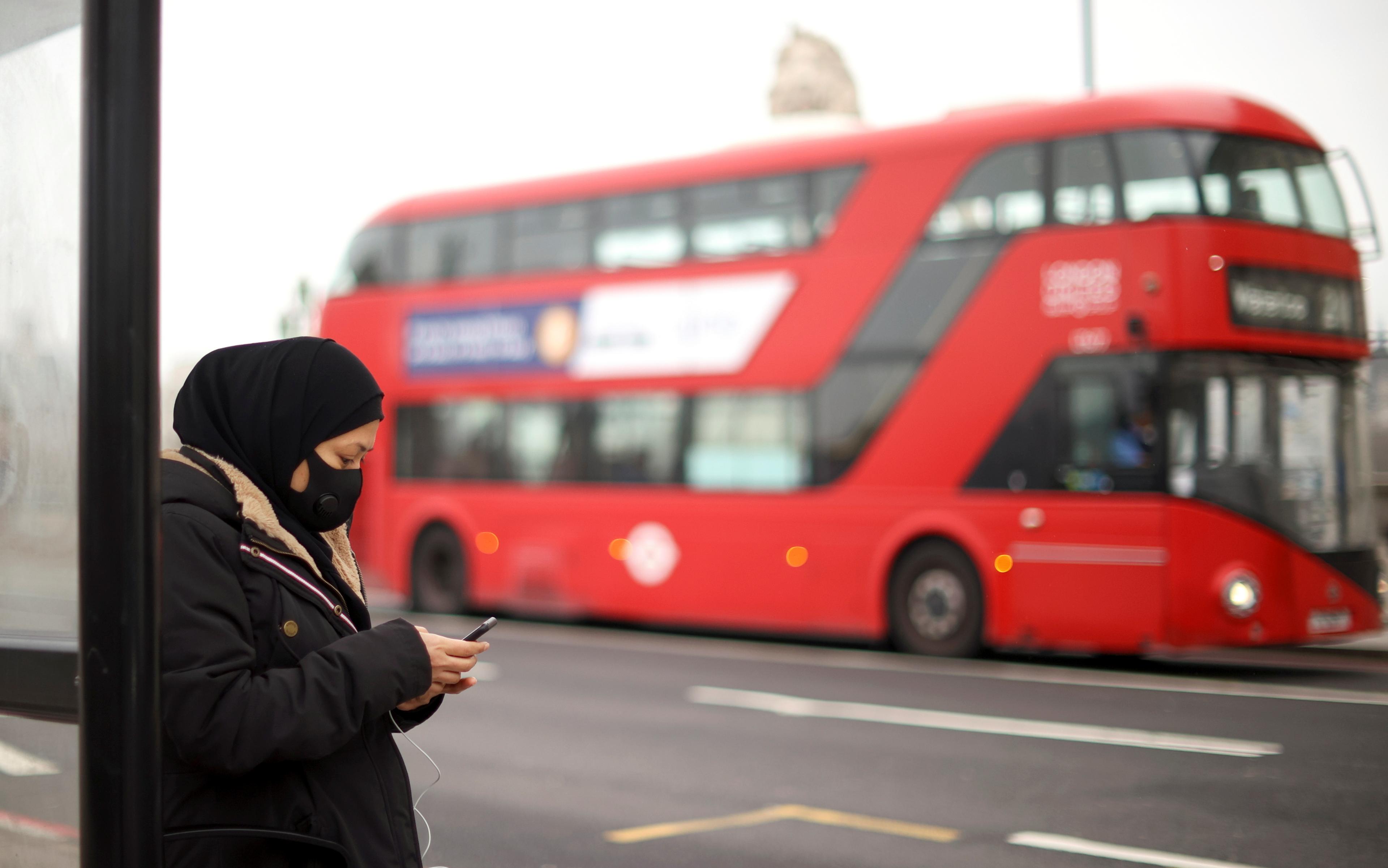 A woman wearing a protective mask uses her mobile at a bus stop