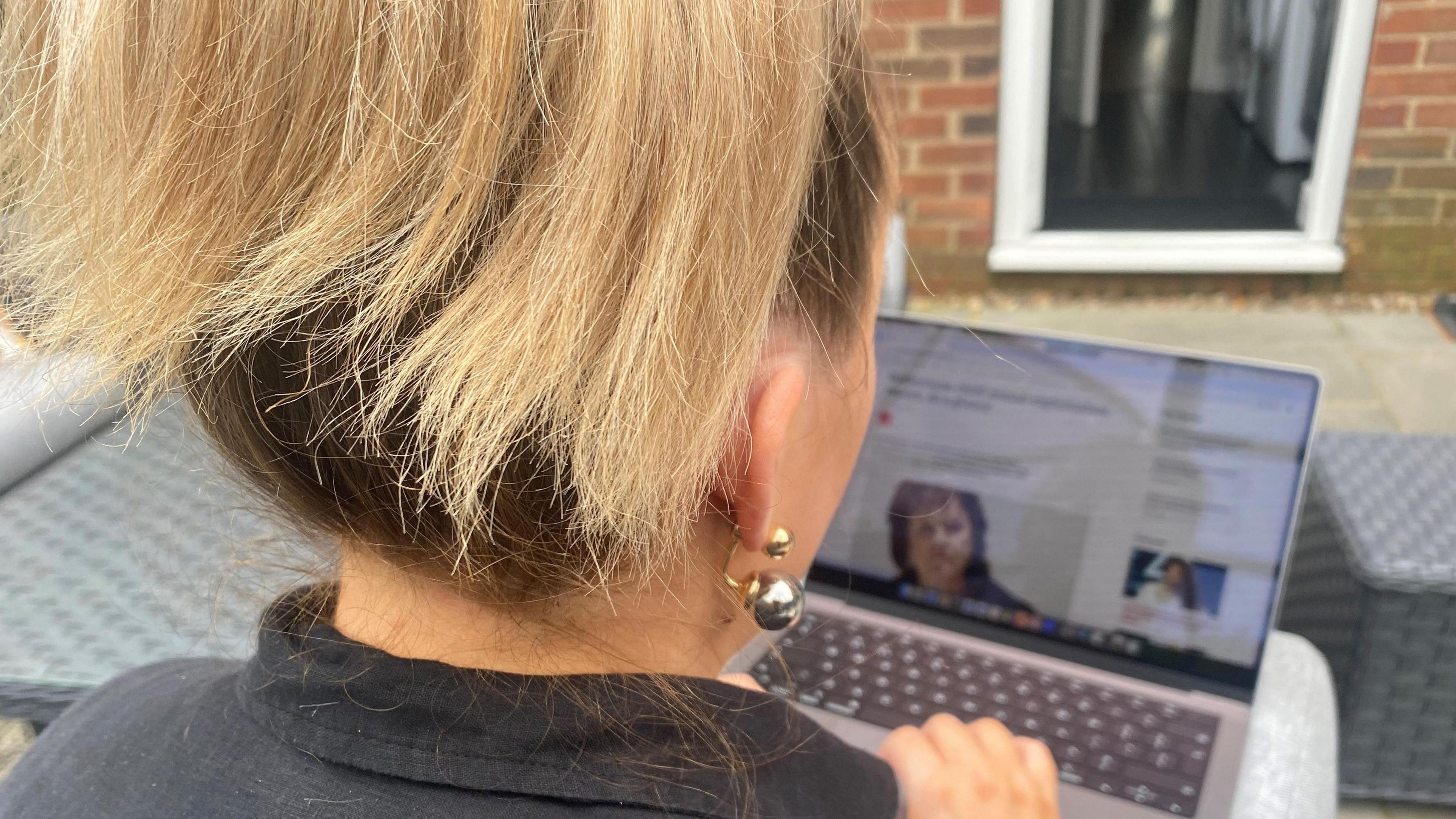 Survivor Amy seen from behind as she reads the news on a laptop. Her face is not visible