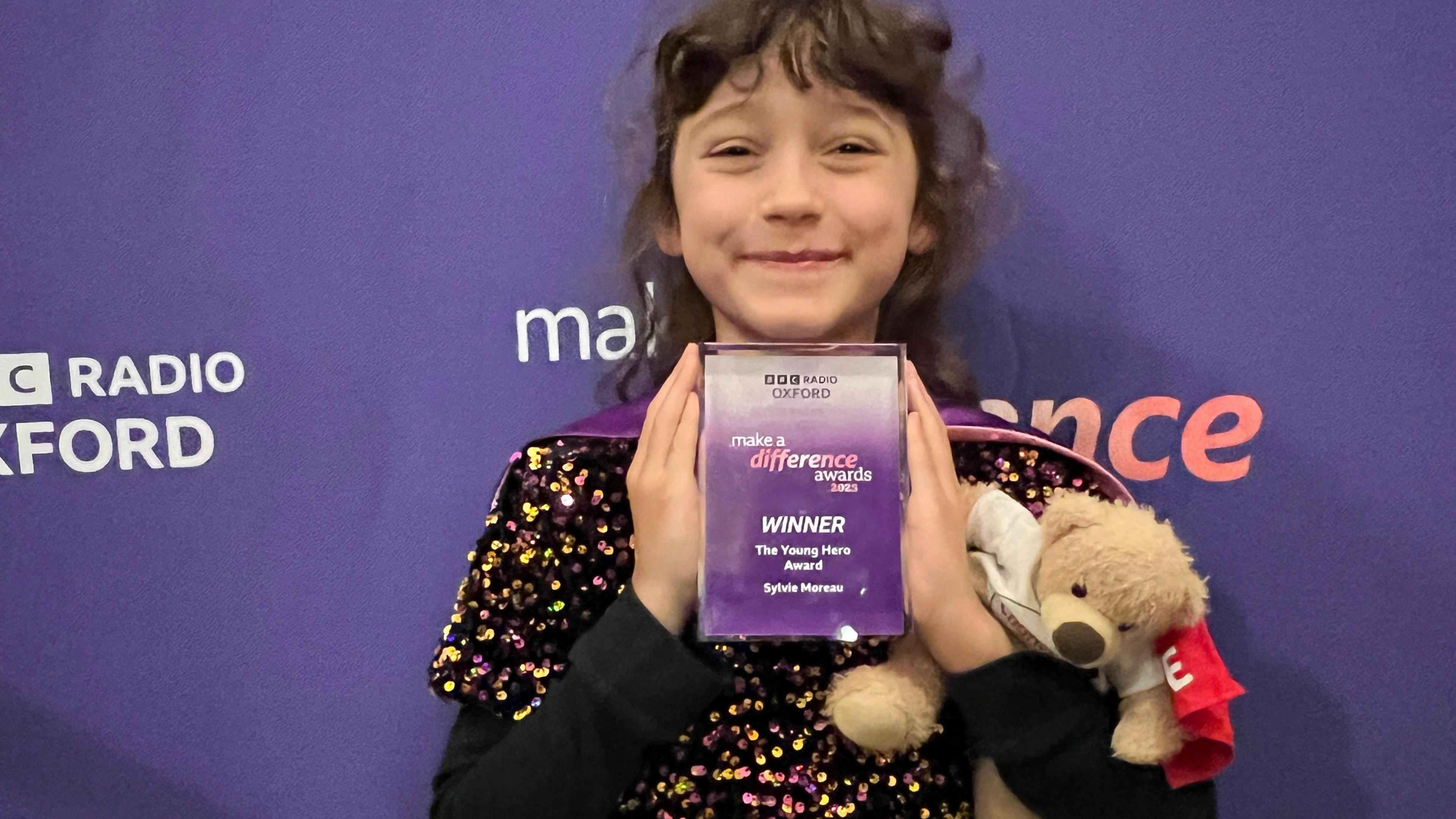 Sylvie, holding a teddy bear, and the award under her chin