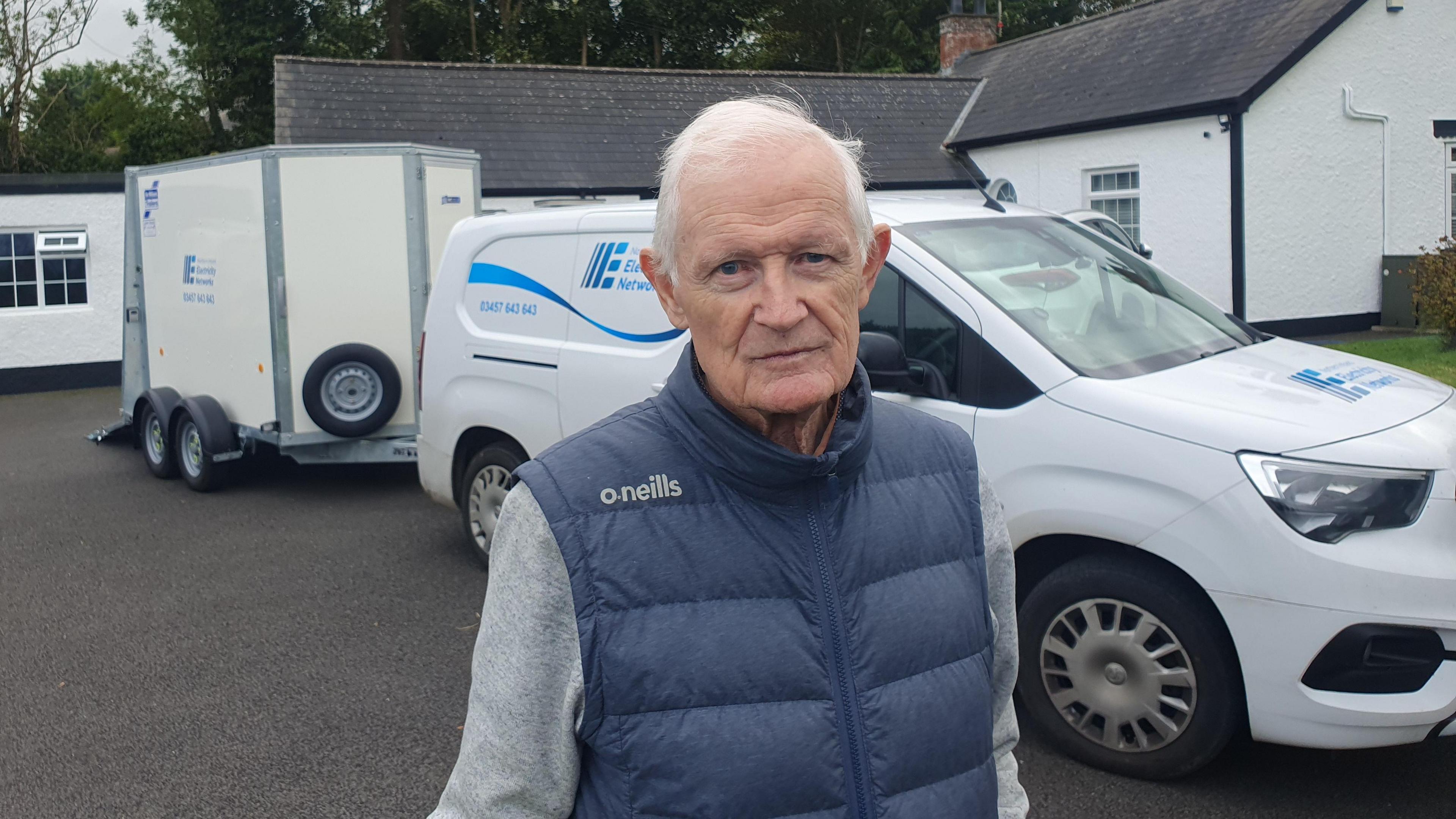 Jimmy O'Reilly wears a blue gilet over a grey long sleeve top. He stands in front of a Northern Ireland Electricity Network van.