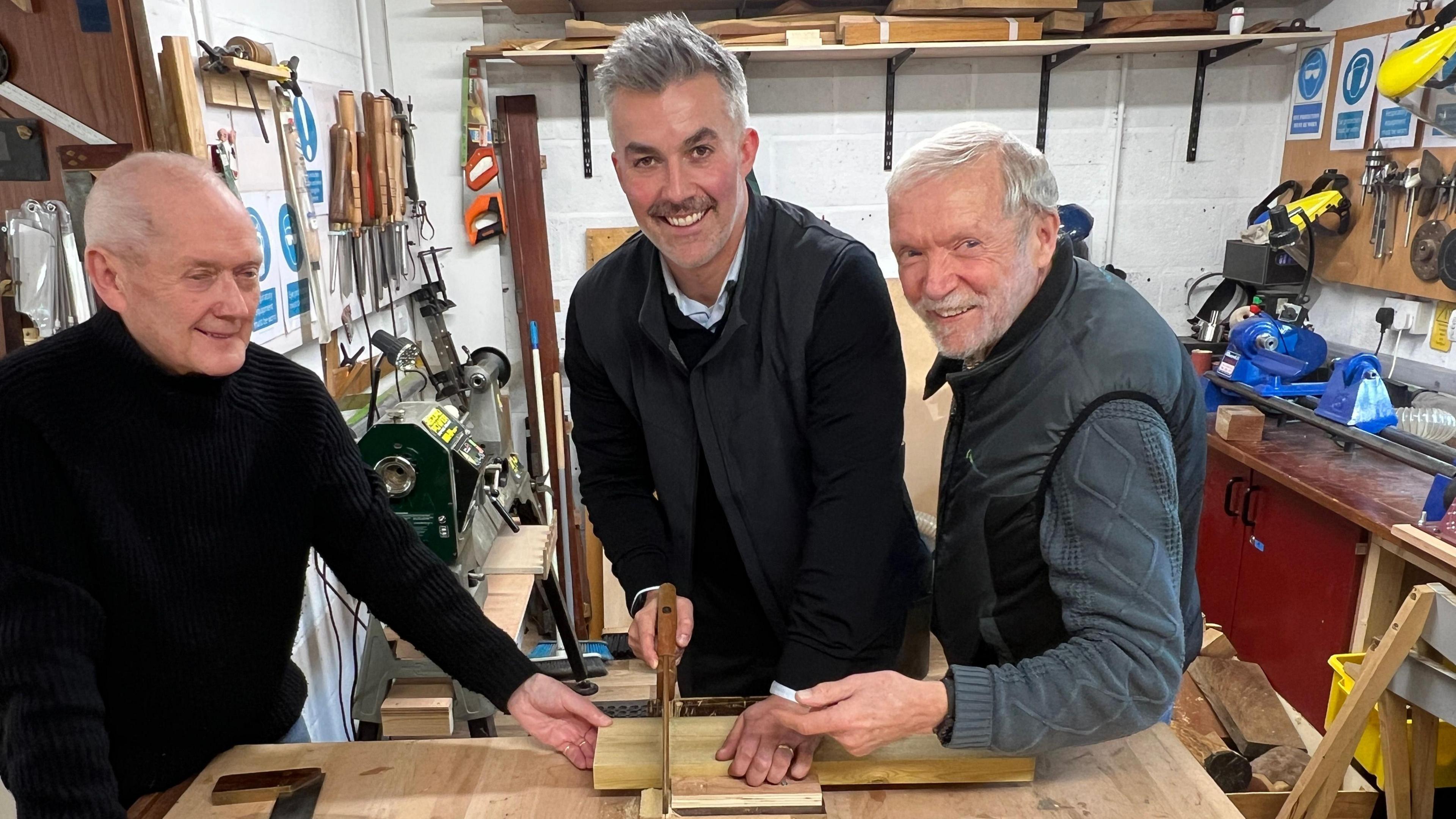 This picture shows elected mayor David Skaith getting a woodwork lesson at York Mens Shed. Mr Skaith is sawing through a block of wood. Shed members Stuart Crossland and Peter Doherty are helping him.