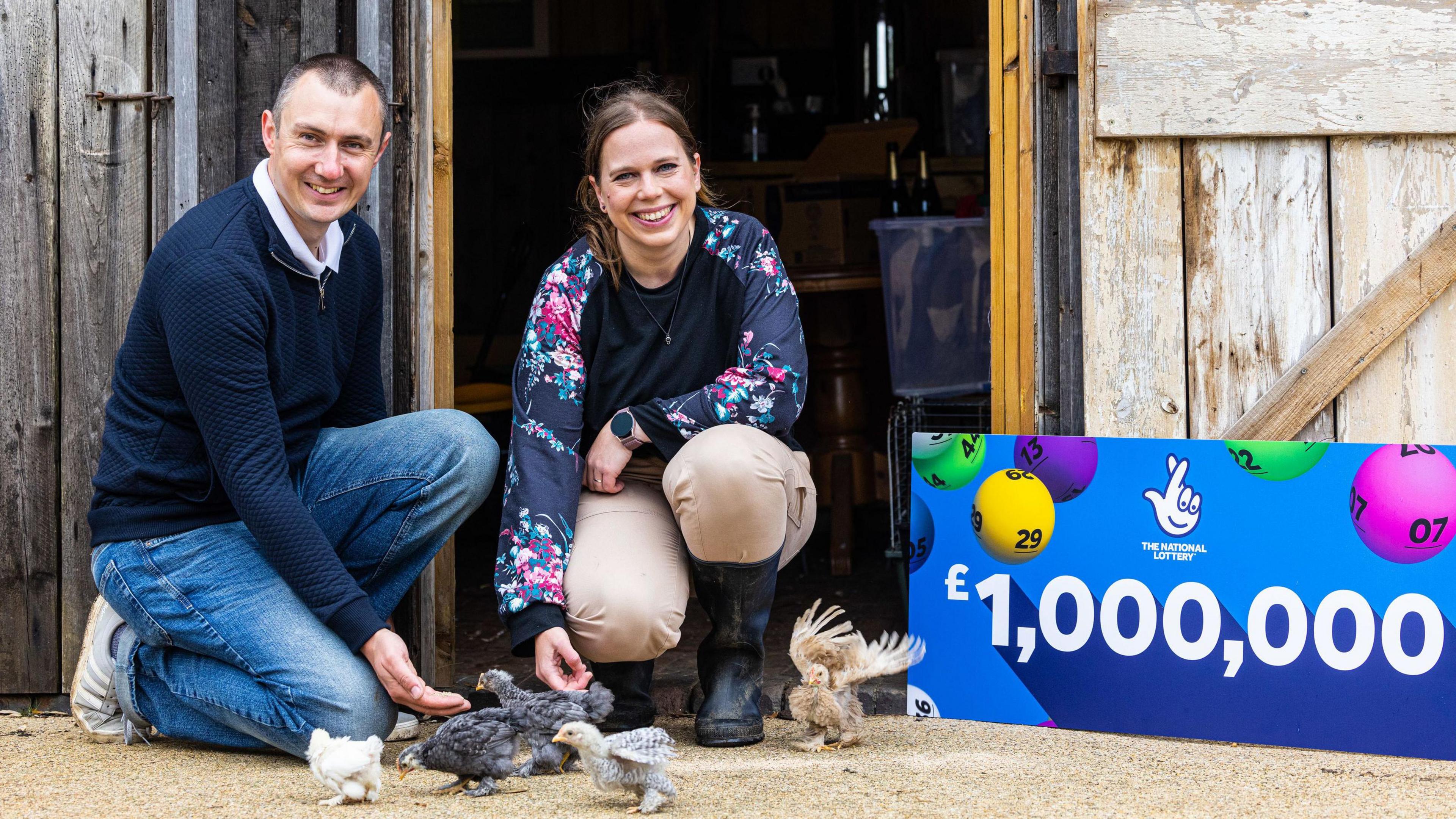 Graeme and Katherine White with bantam hens and a £1m Lottery sign in front of a barnd 