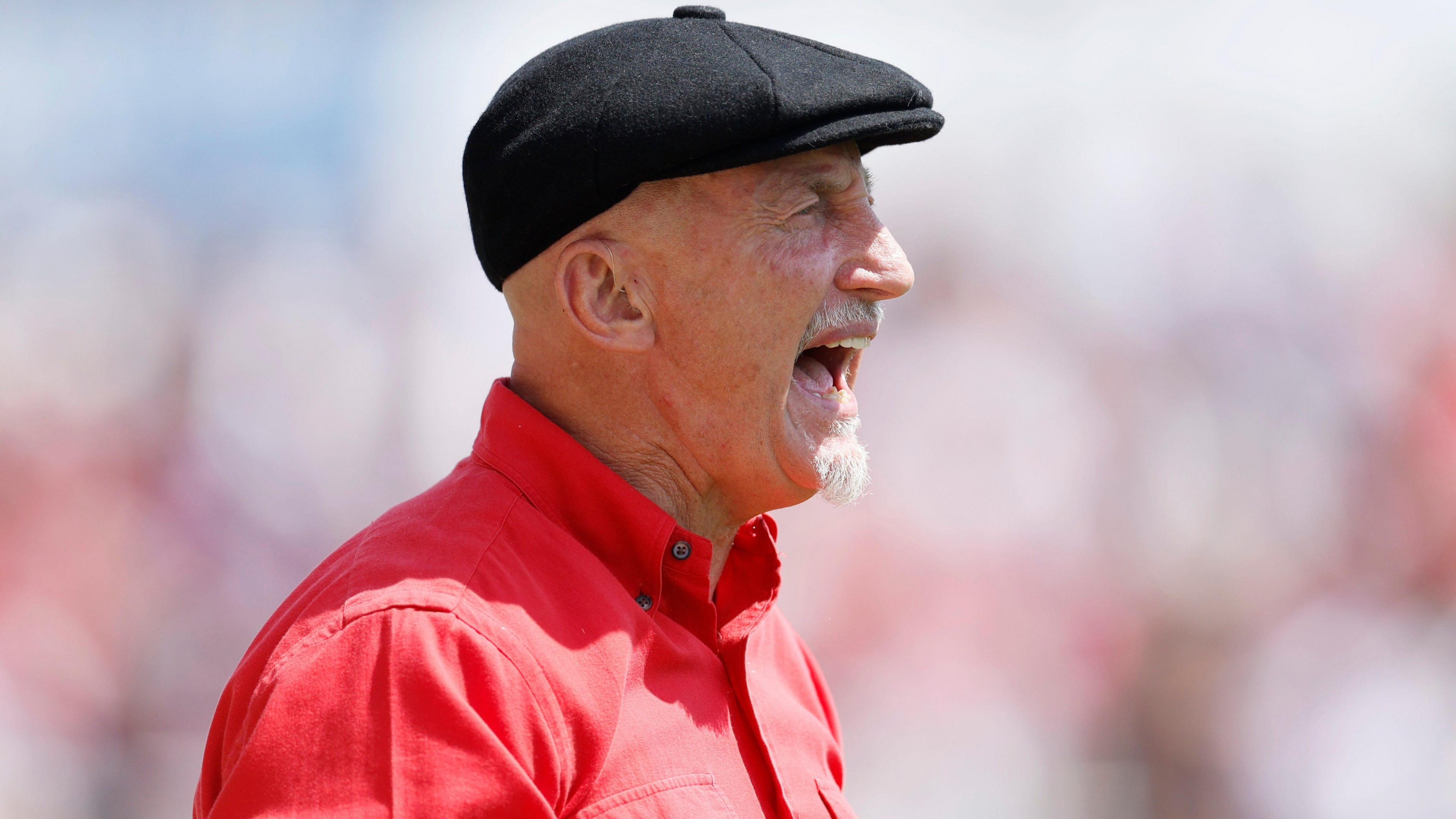 Ian Holloway, wearing a black flat cap and red smart shirt, shouts during a pre-season friendly between Swindon Town and Bristol City in July 2026