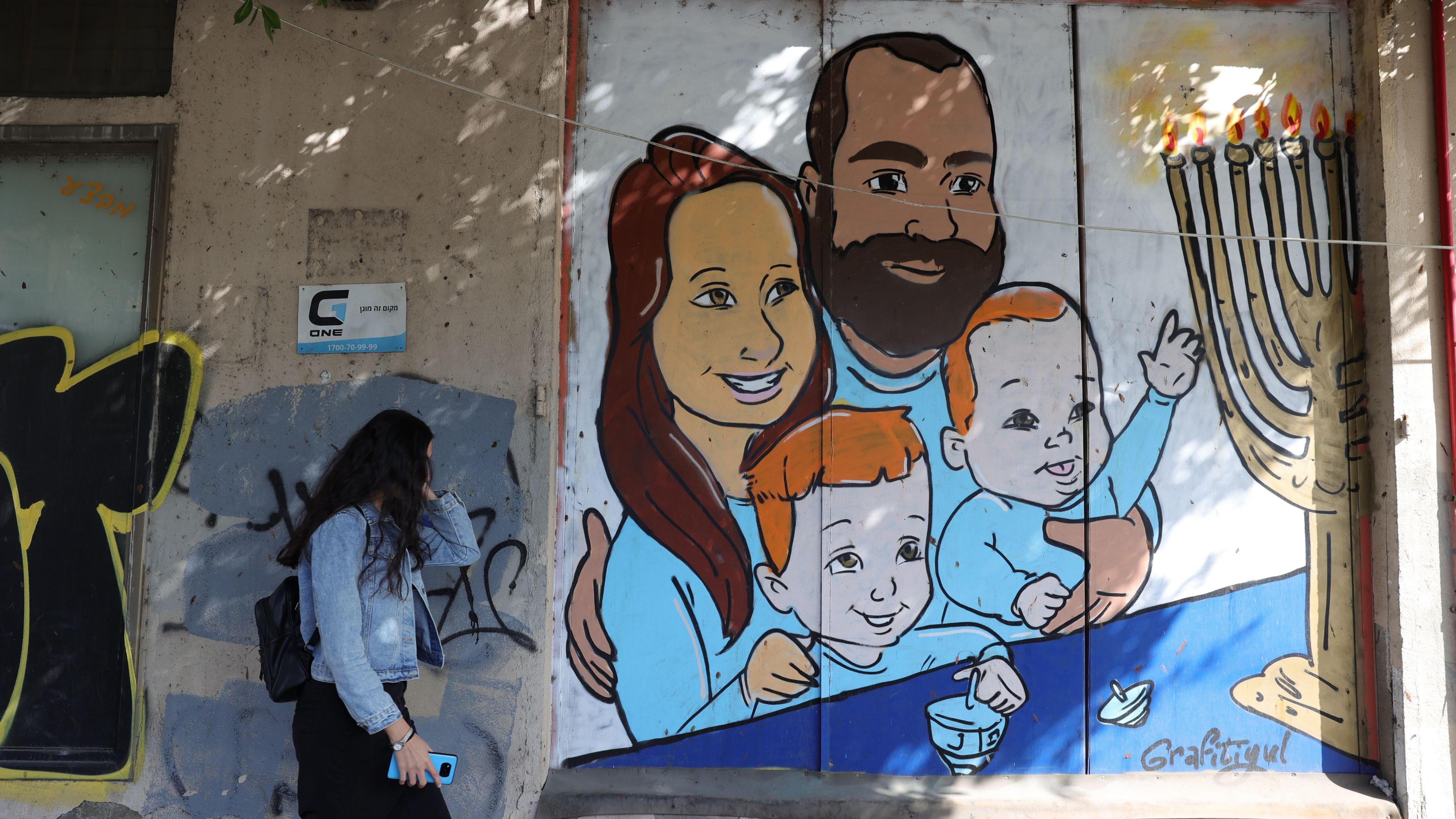 A woman walks past a street artwork depicting the Bibas family on a wall in Tel Aviv