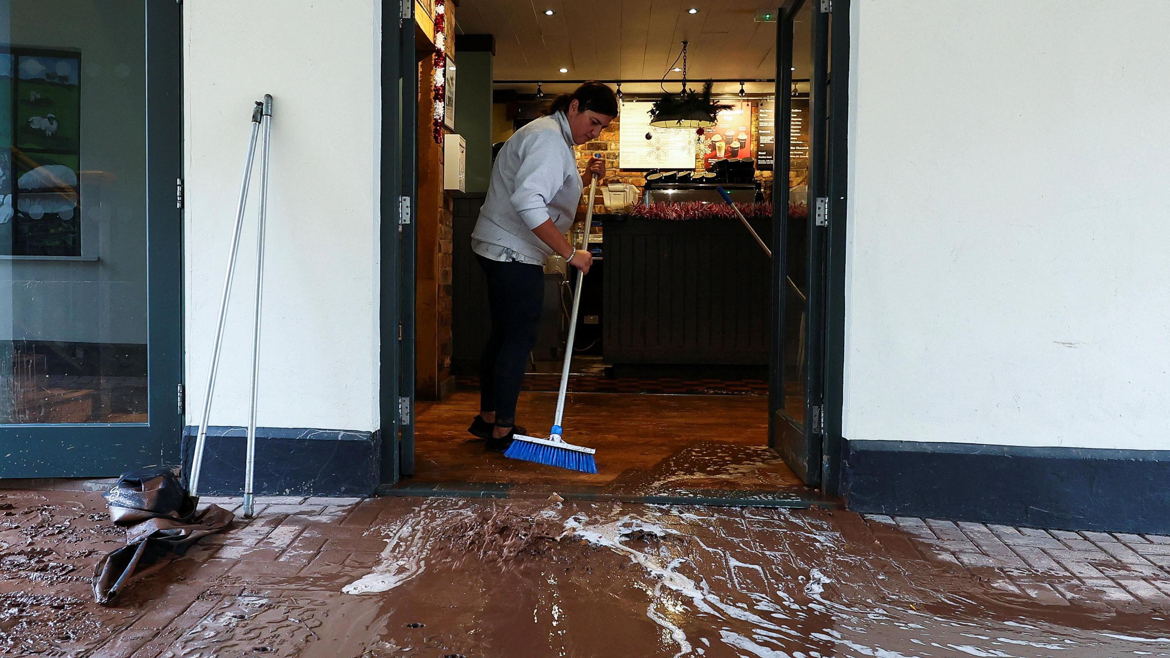 A woman sweeps water away from a coffee shop after severe flooding caused by Storm Claudia, in Monmouth, Wales