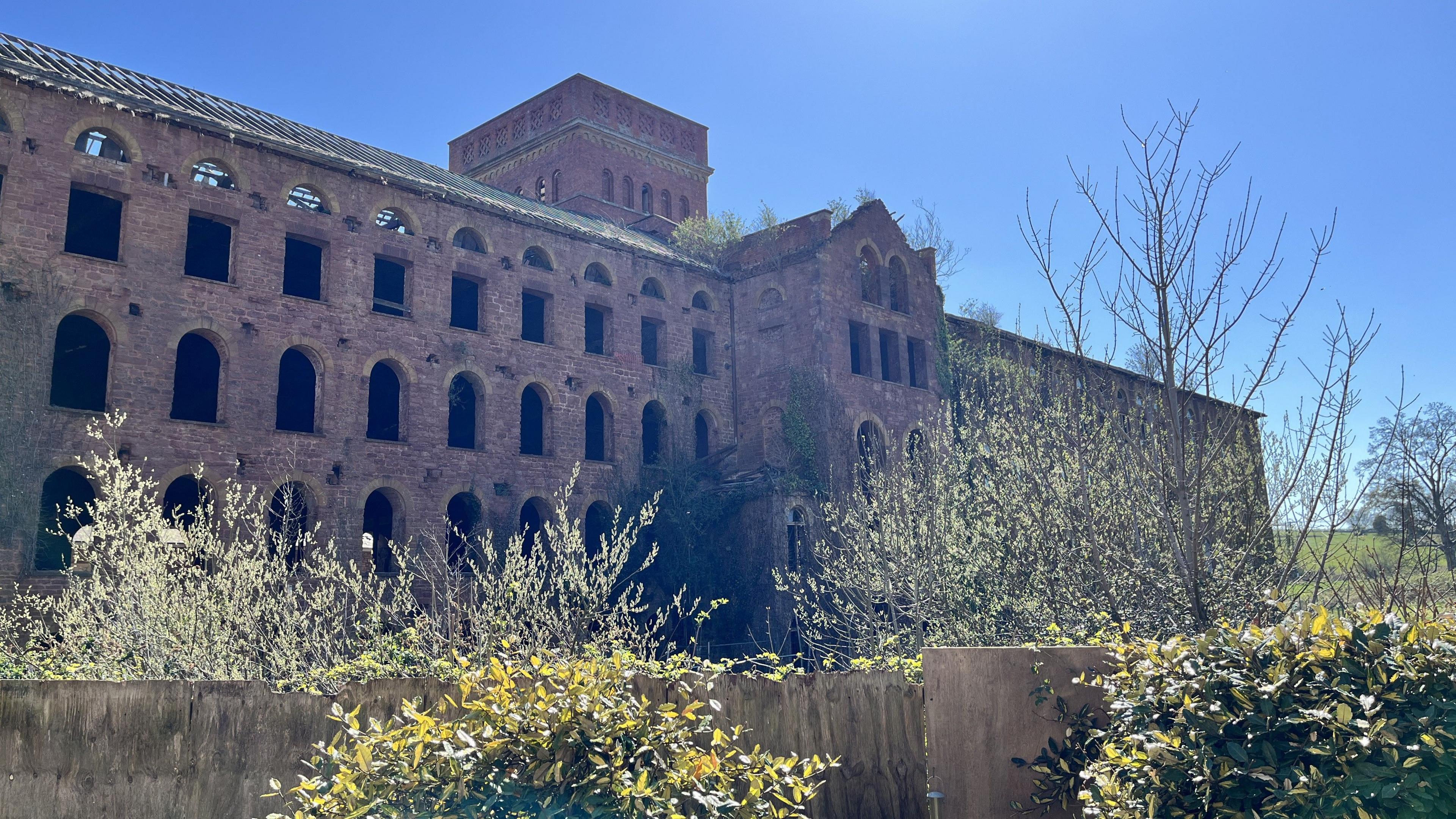 A three-storey brown brick building stretches out for around 100 metres or so into a field. There are entire rows of broken windows. 