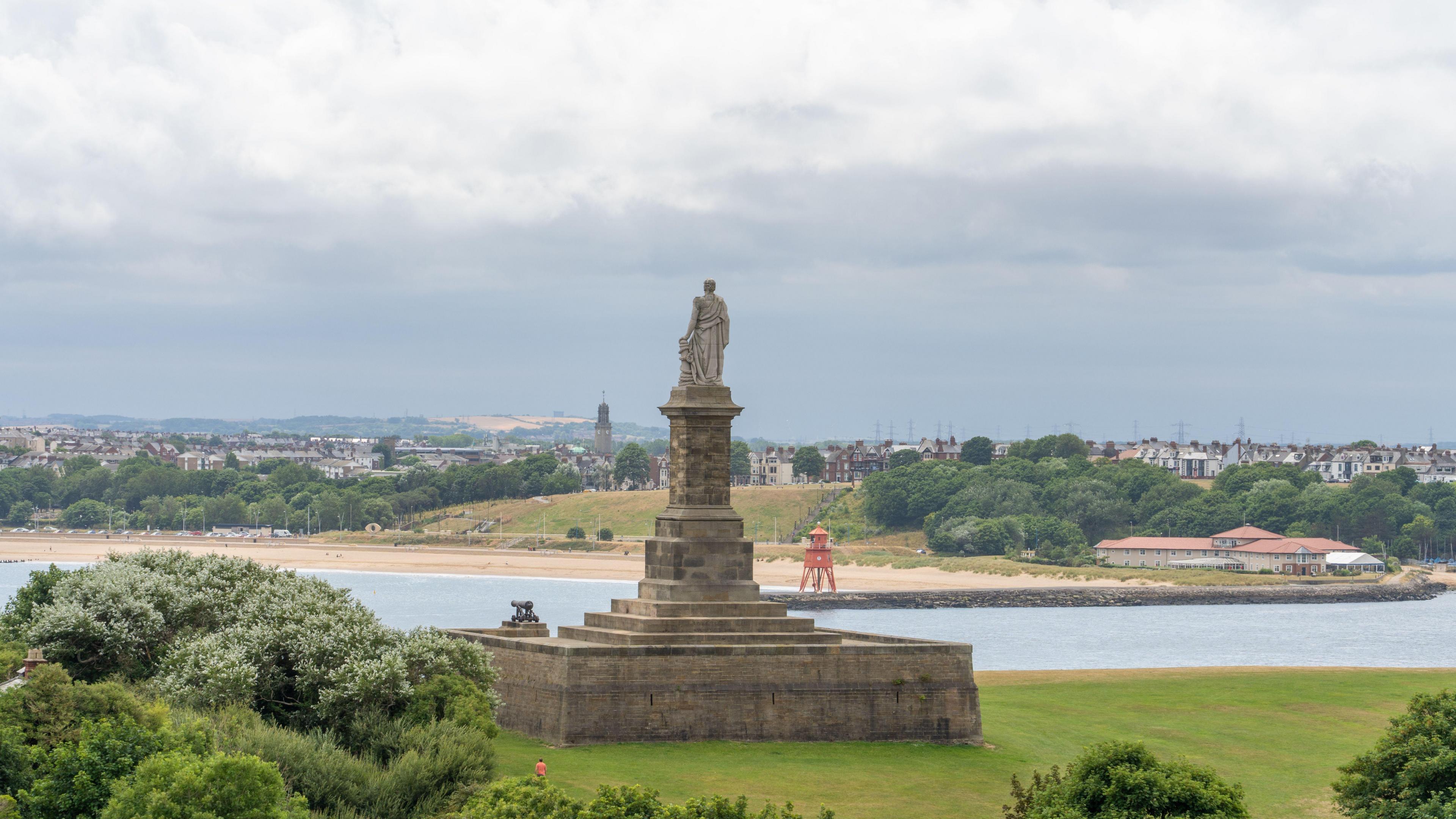 The Collingwood monument in Tynemouth. It's a stone plinth with a man on top.  The sea and a beach can be seen in front of it.