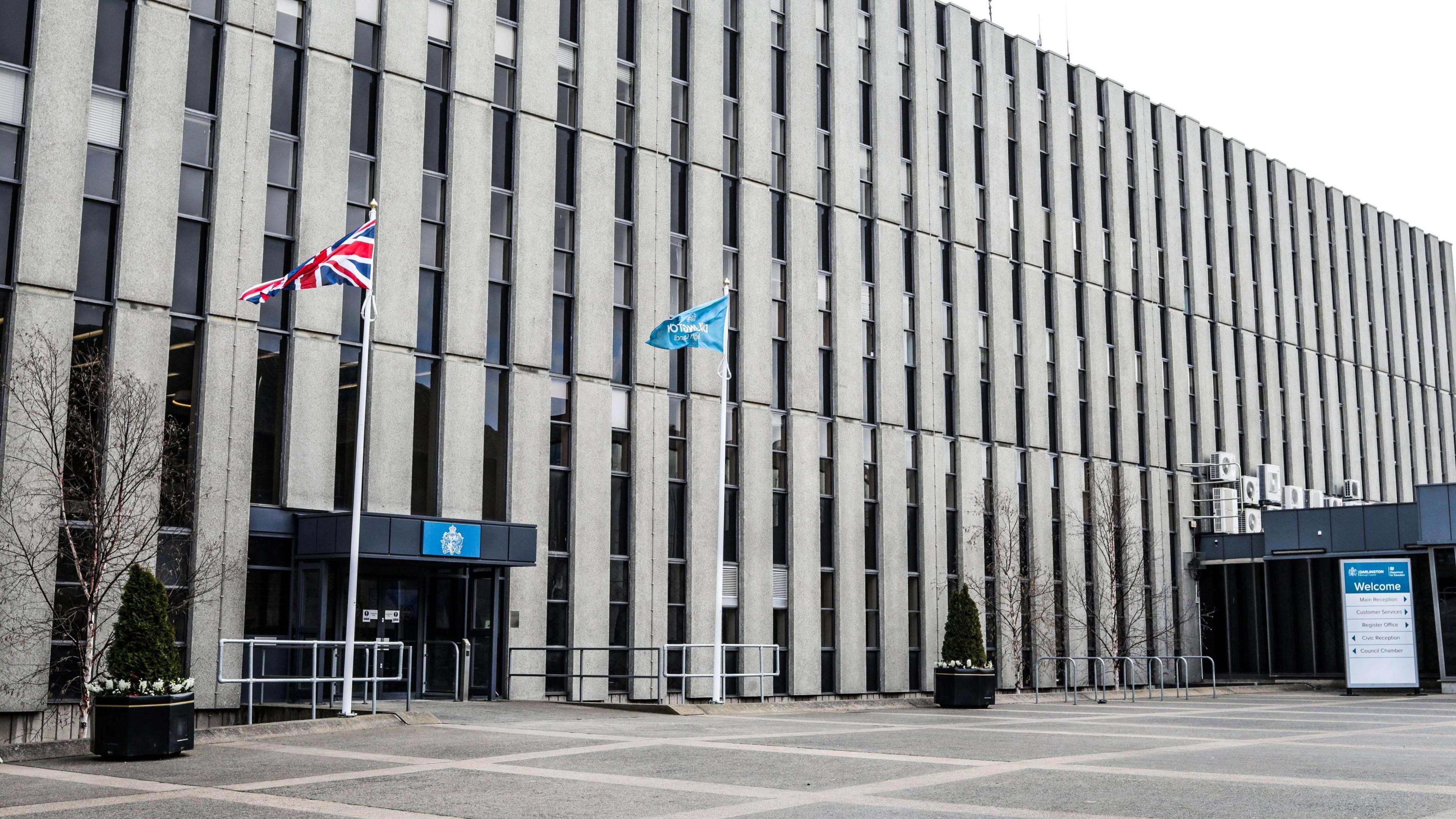 The outside of the Darlington council building. It is a large concrete building with two flag poles outside.