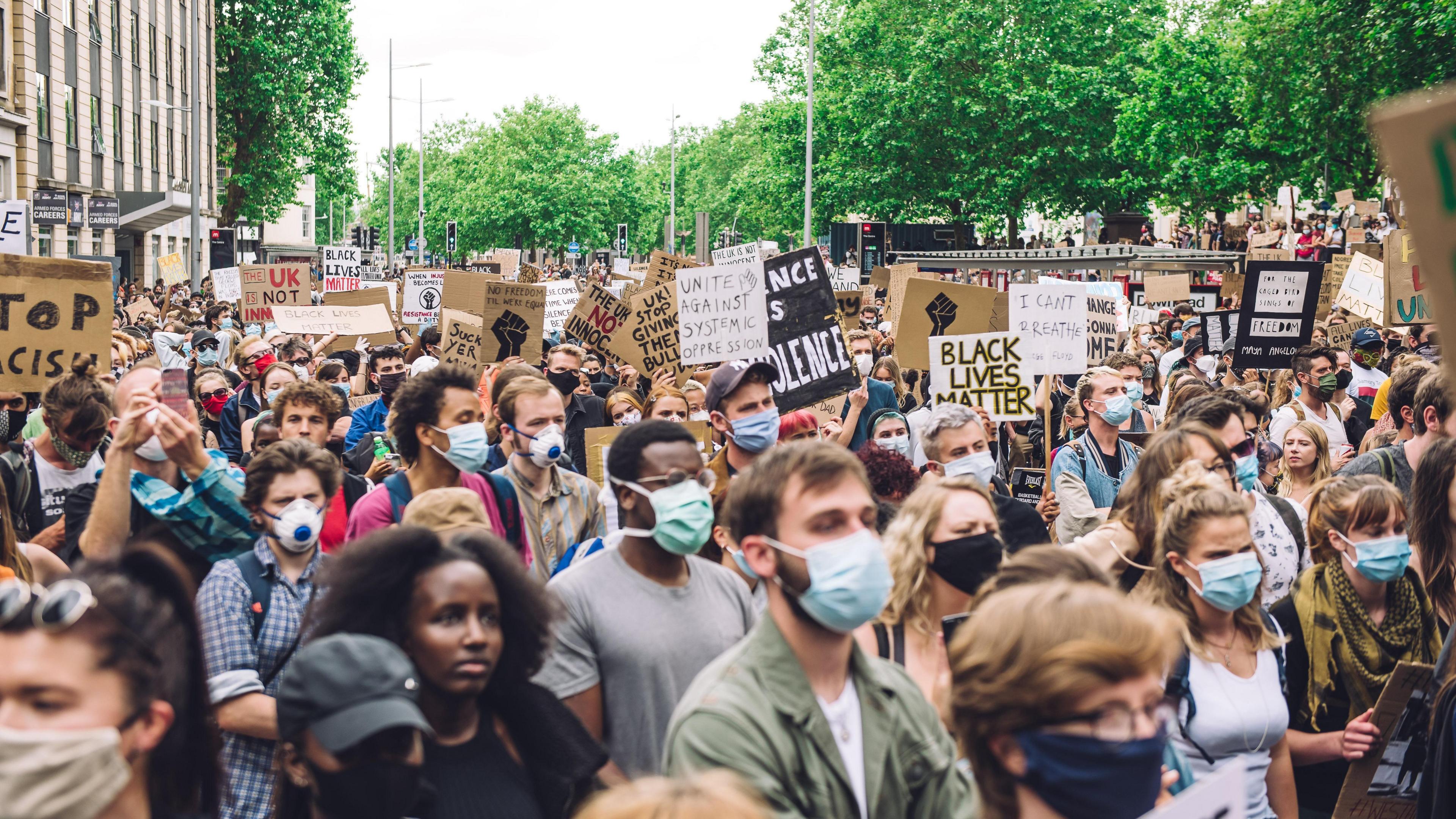 A large crowd of people at a Black Lives Matter protest in Bristol. Many of them are wearing face masks and carrying signs calling for an end to racism.