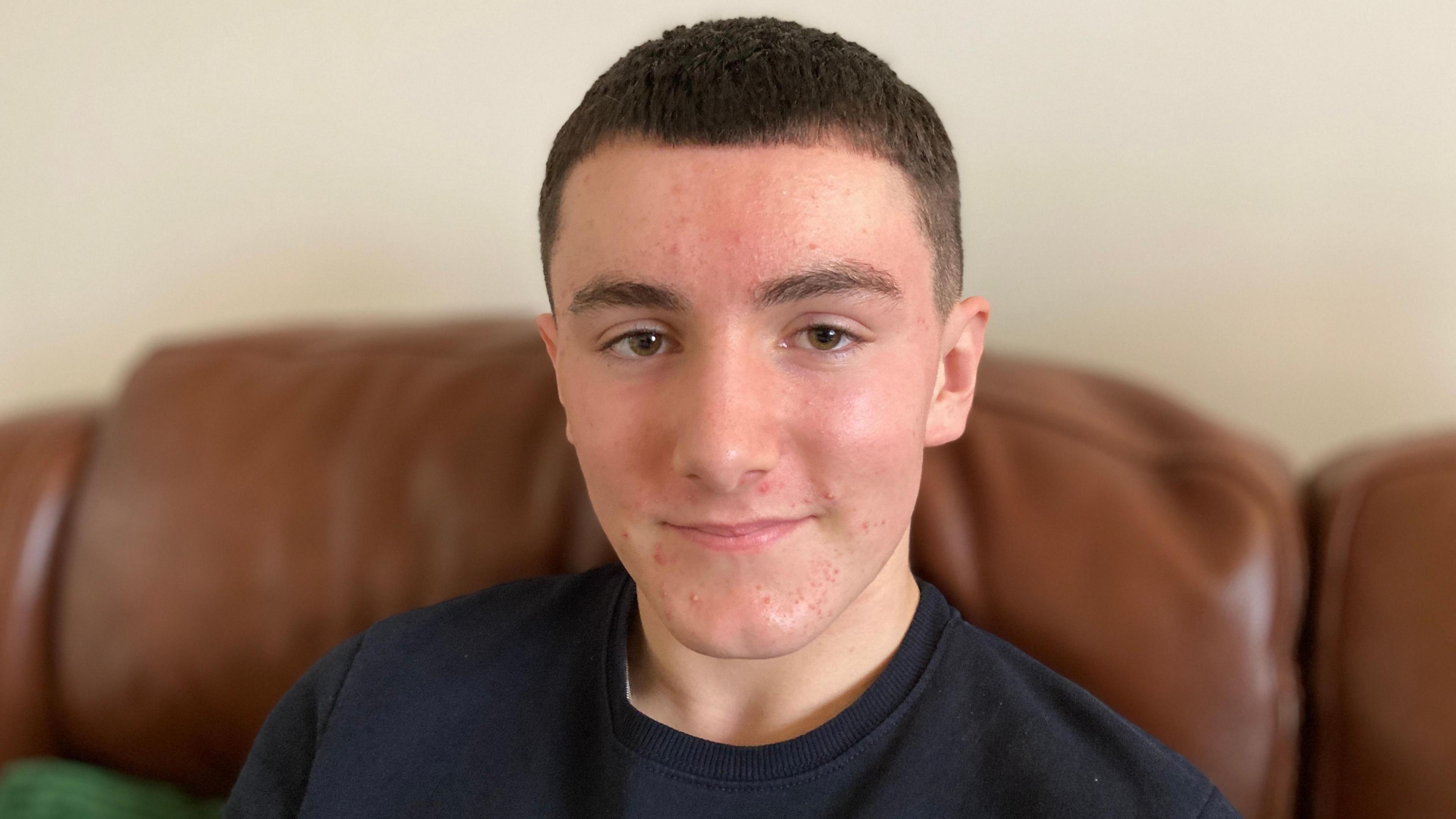 Teenager Will is smiling and looking directing into camera. He has short dark brown hair and is wearing a dark blue T-shirt.