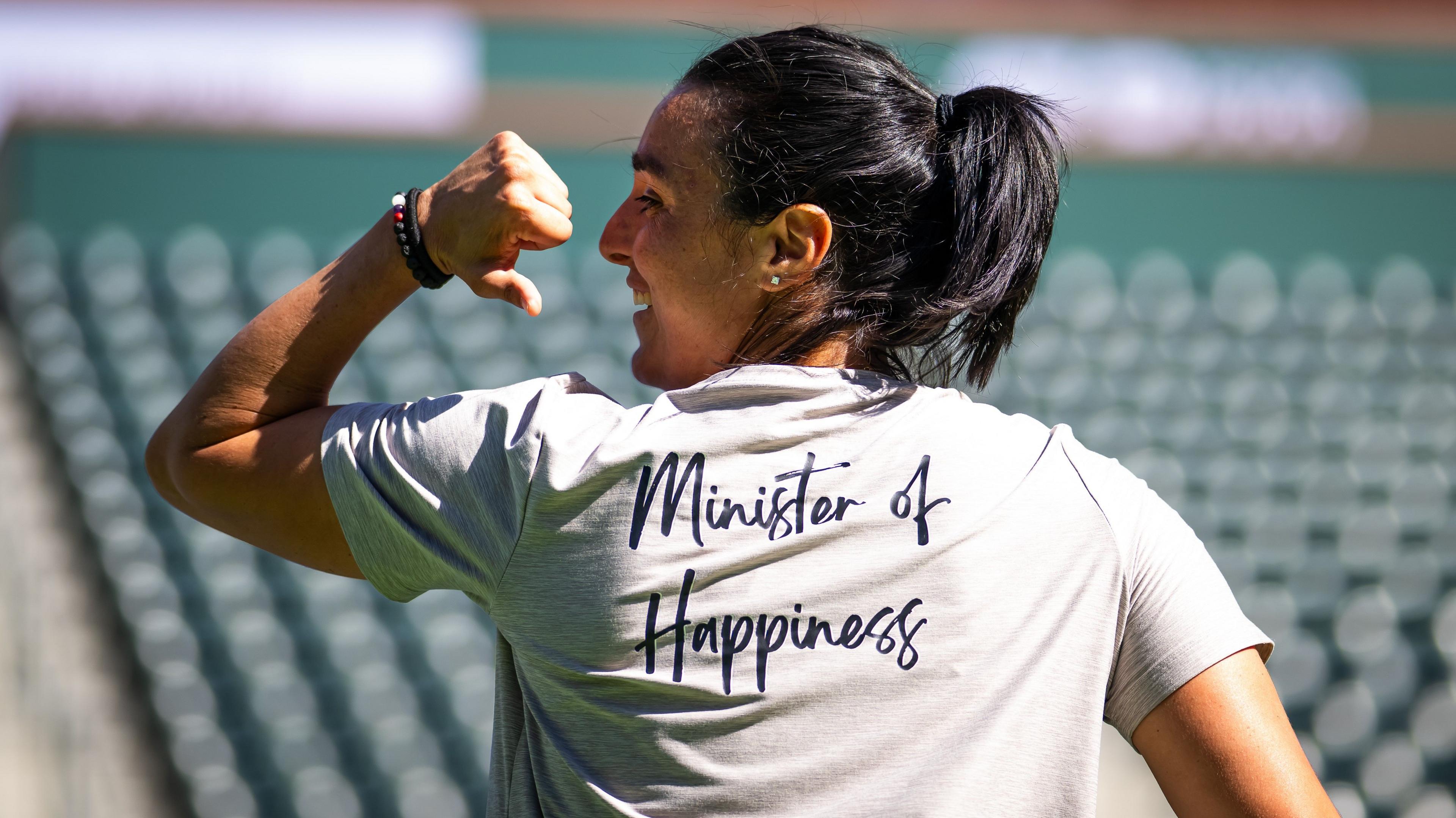 Tunisian tennis star Ons Jabeur pointing to the back of her t-shirt which has the words "Minister of Happiness" written on it.