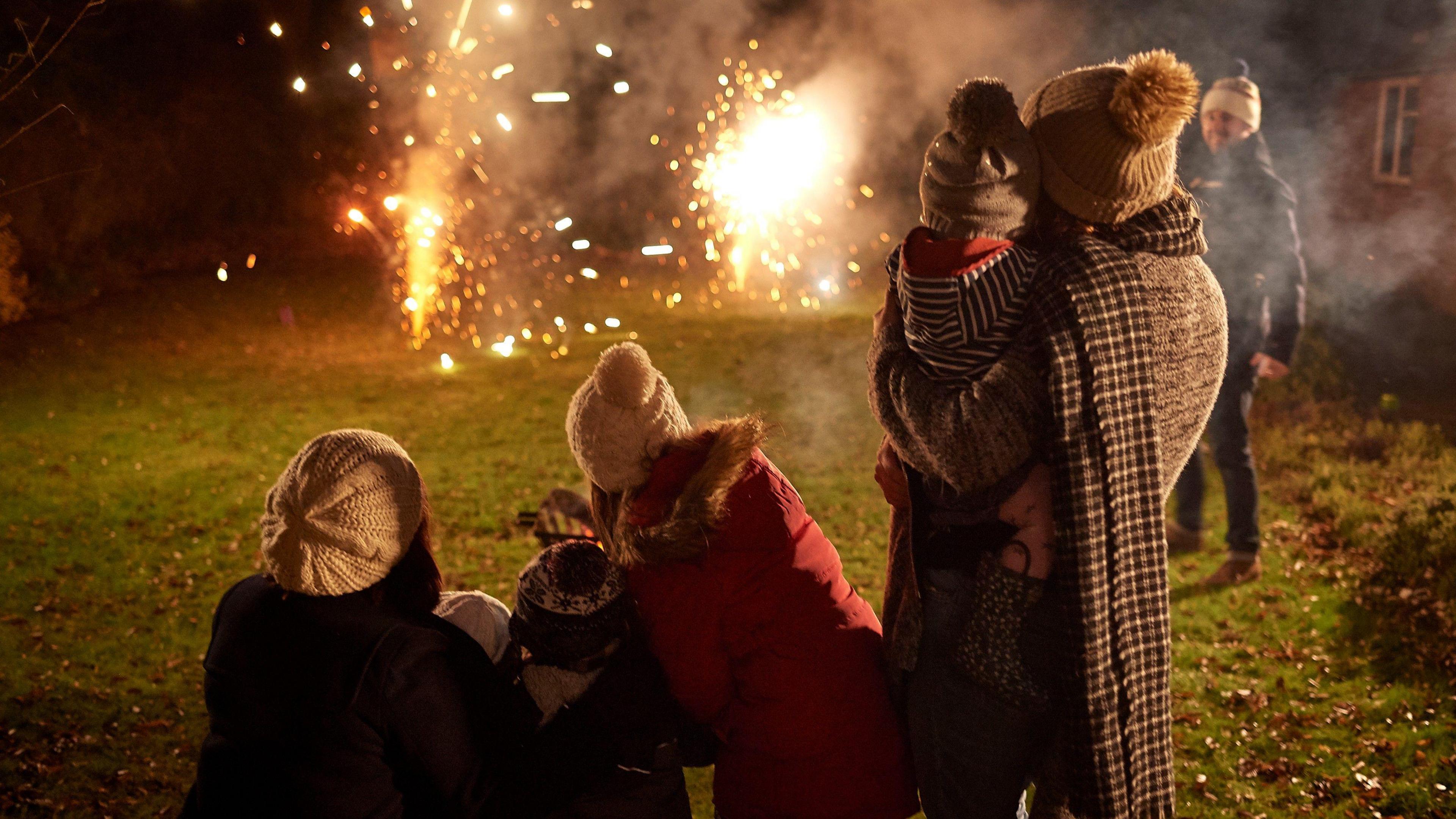 A family wearing outdoor clothing watching a Bonfire Night fireworks display.