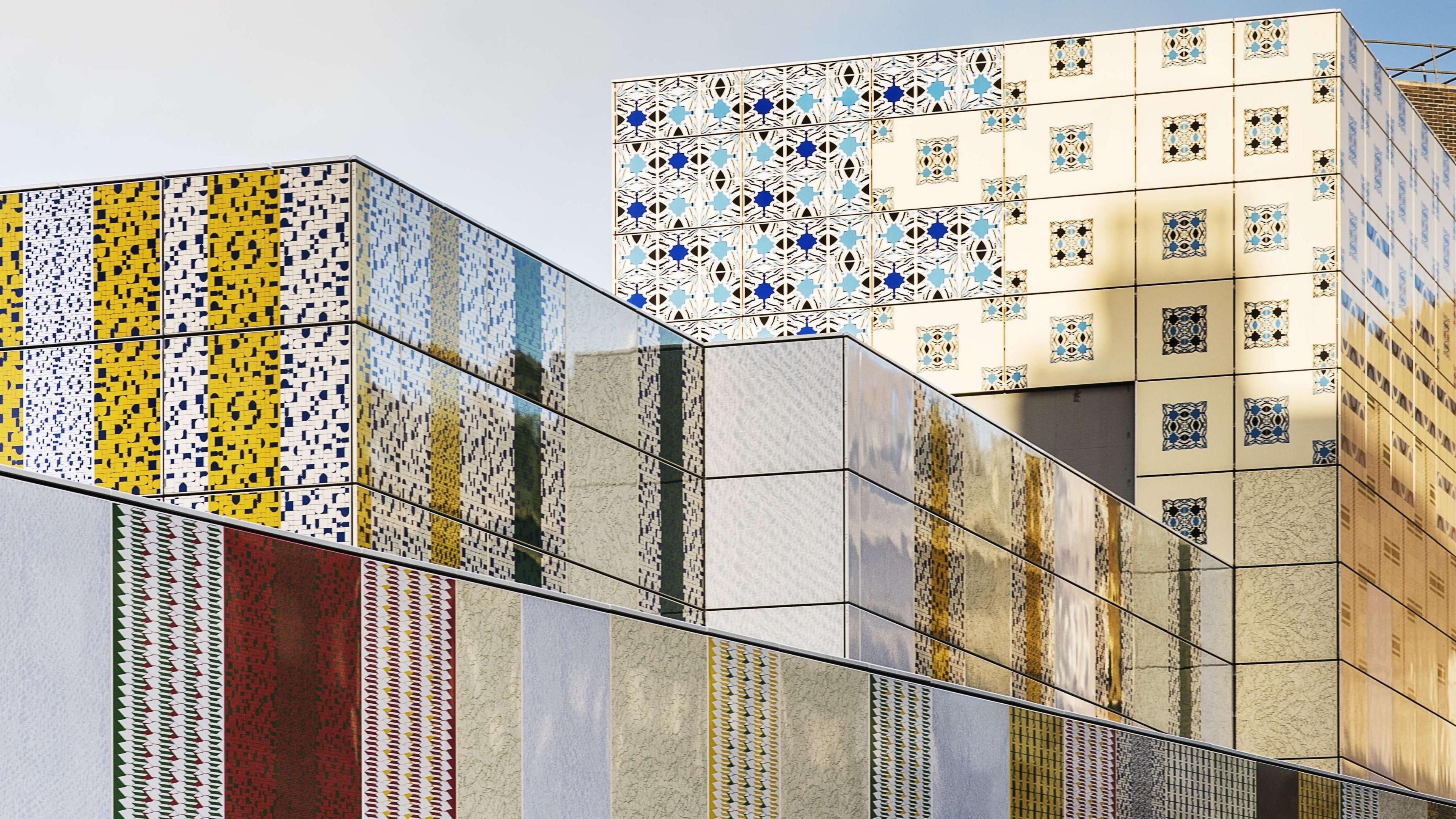 The outside of a Tube station with large rooftop blocks wrapped in an enamel covering with various patterns reminiscent of Middle Eastern designs, in blue, black, white and yellow. 