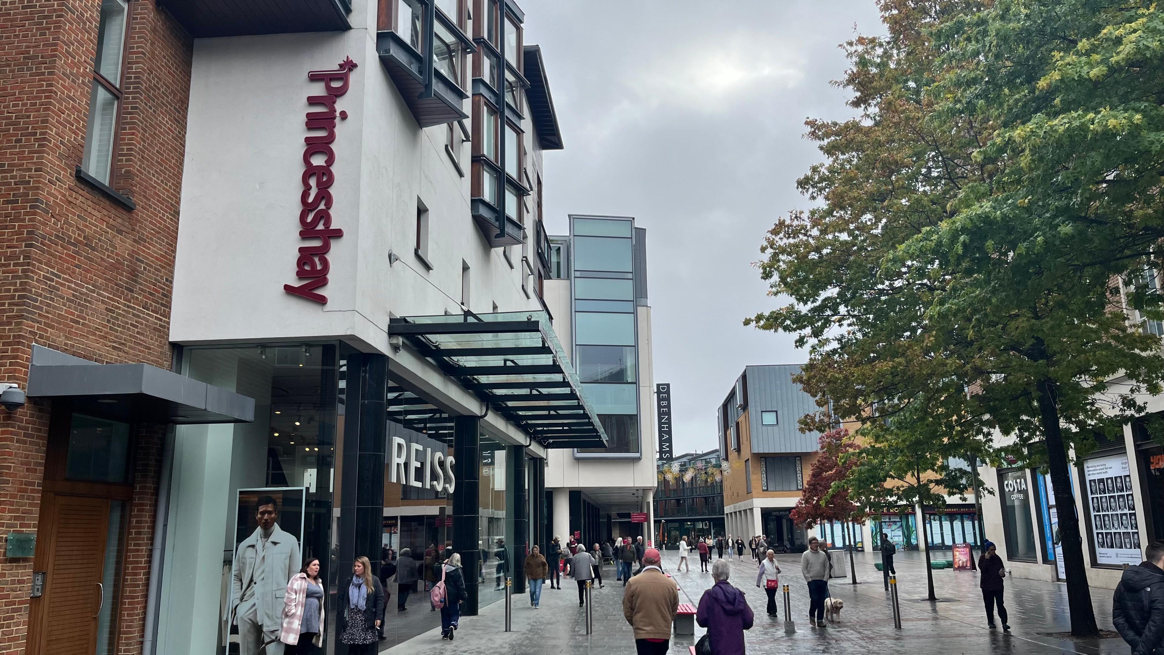 People walking in the Princesshay area of Exeter with the Princesshay sign on the left above the Reiss shop