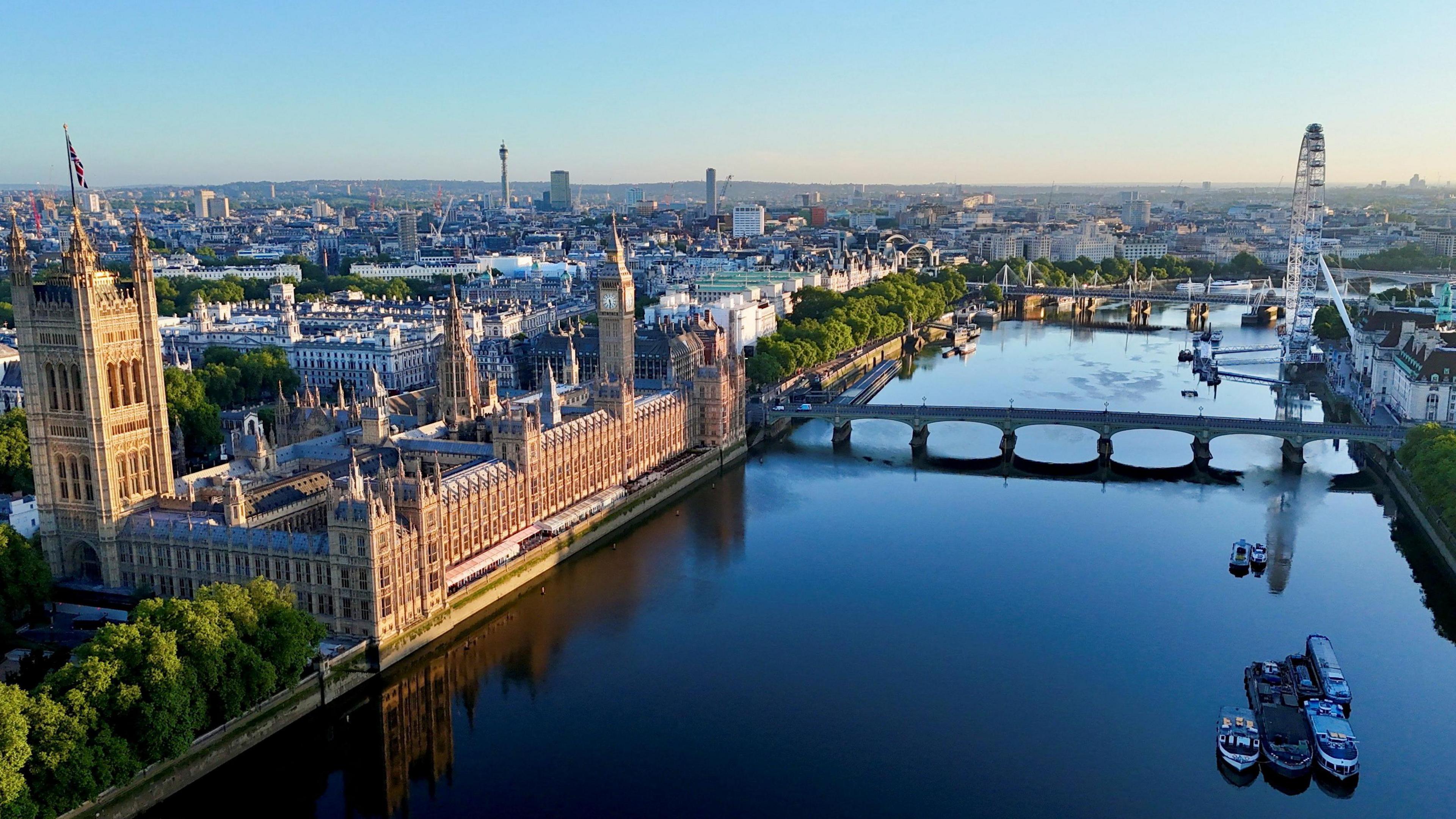 An aerial photo of a June morning in summer featuring the London Eye, a ferris wheel on the South Bank, the Houses of Parliament and the River Thames. 