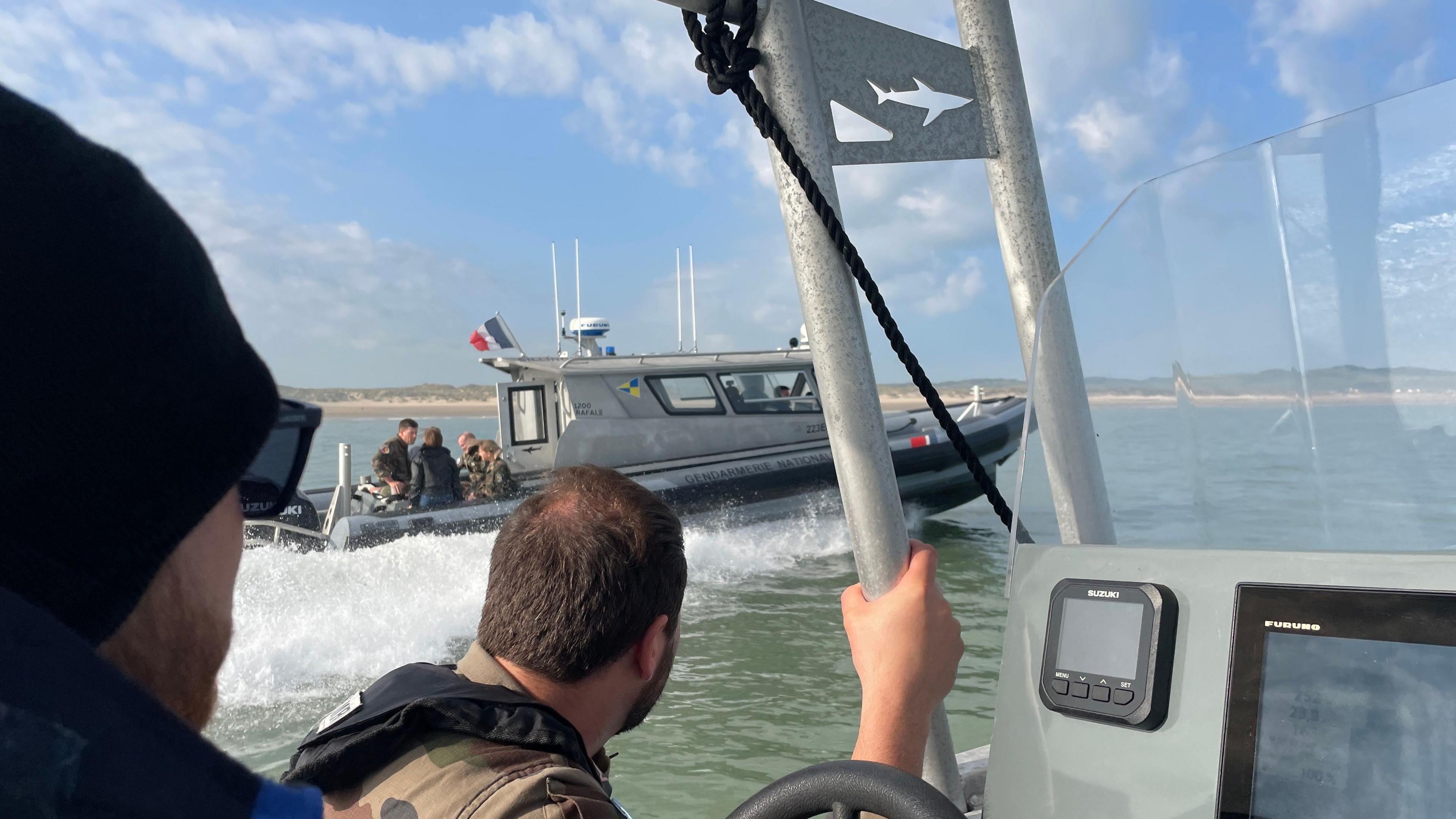 Two men sit in the patrol boat, with a second patrol boat on the water across from them