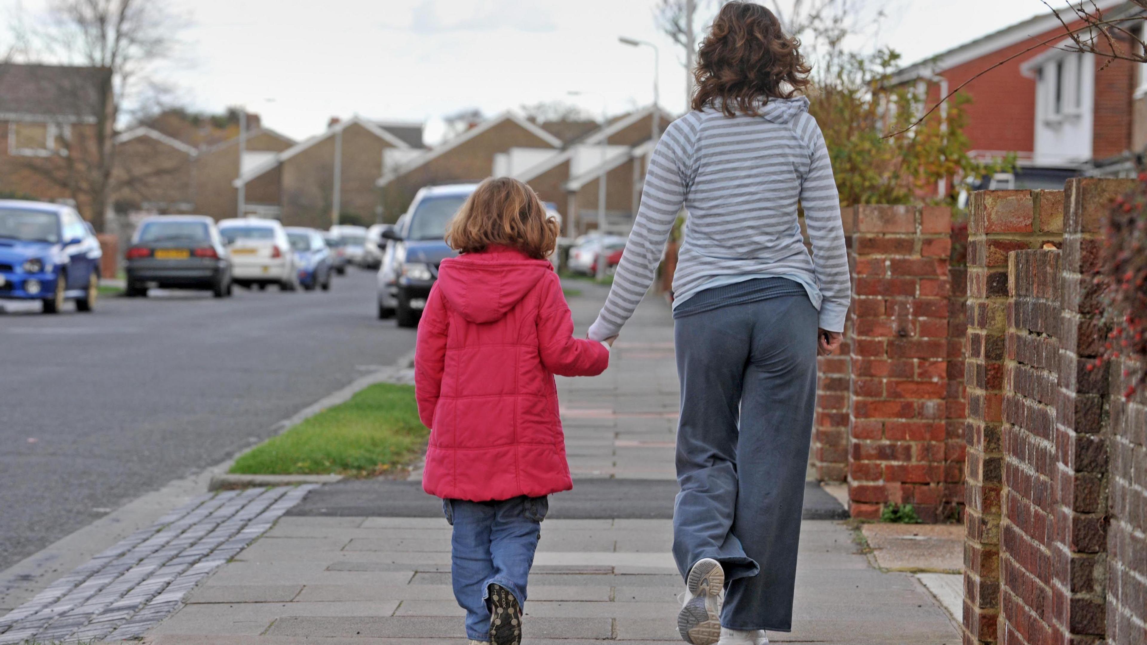 Rear view of a woman and a young girl walking on a residential street holding hands