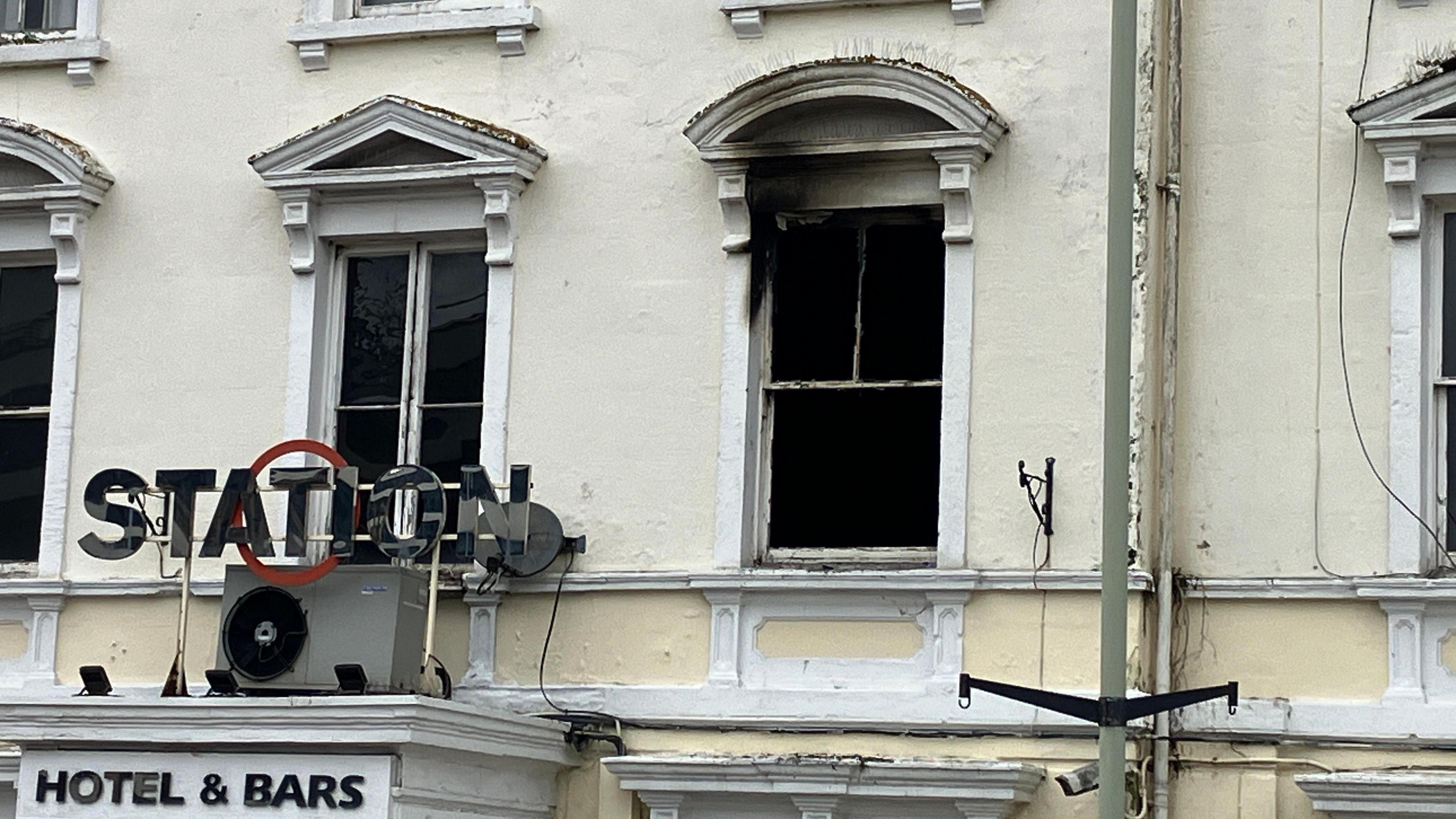 A close-up, exterior view of the Station Hotel. The windows are smashed and marks left by black smoke can be seen on the outside. 