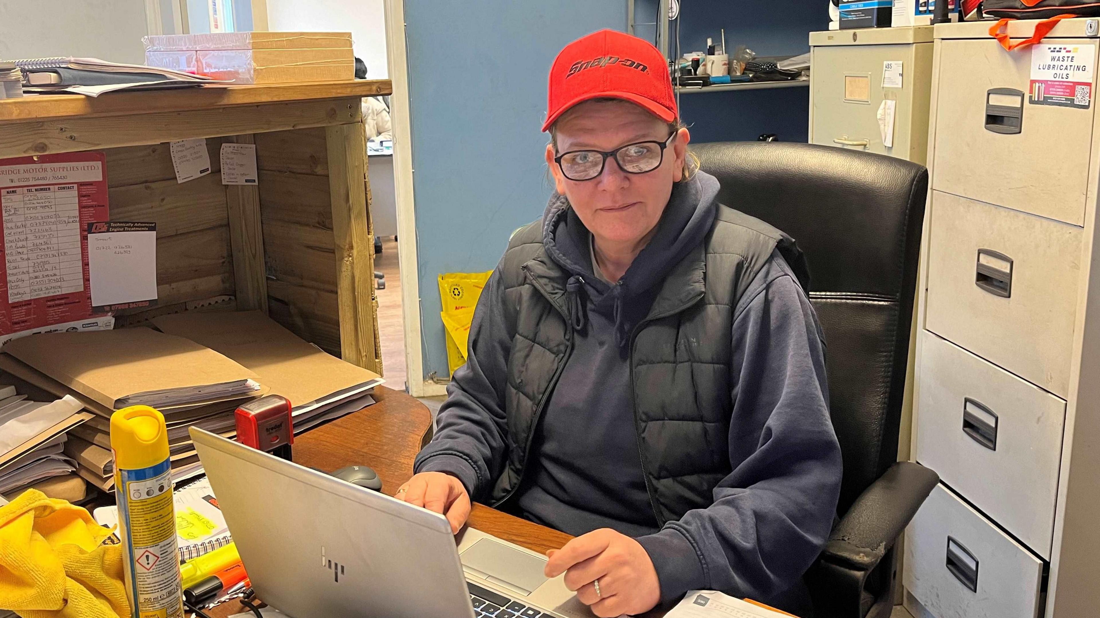 Tracy Lloyd wears glasses and a red baseball cap and is pictured at her desk at the garage.