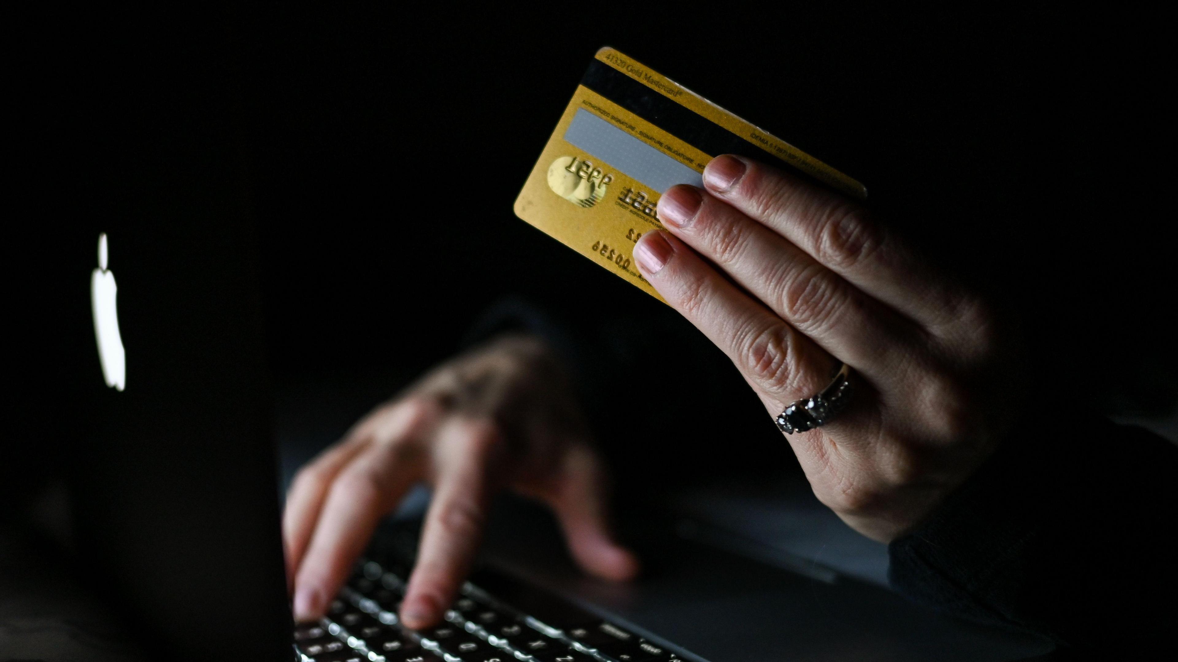 A woman holds a gold credit card while typing on a laptop