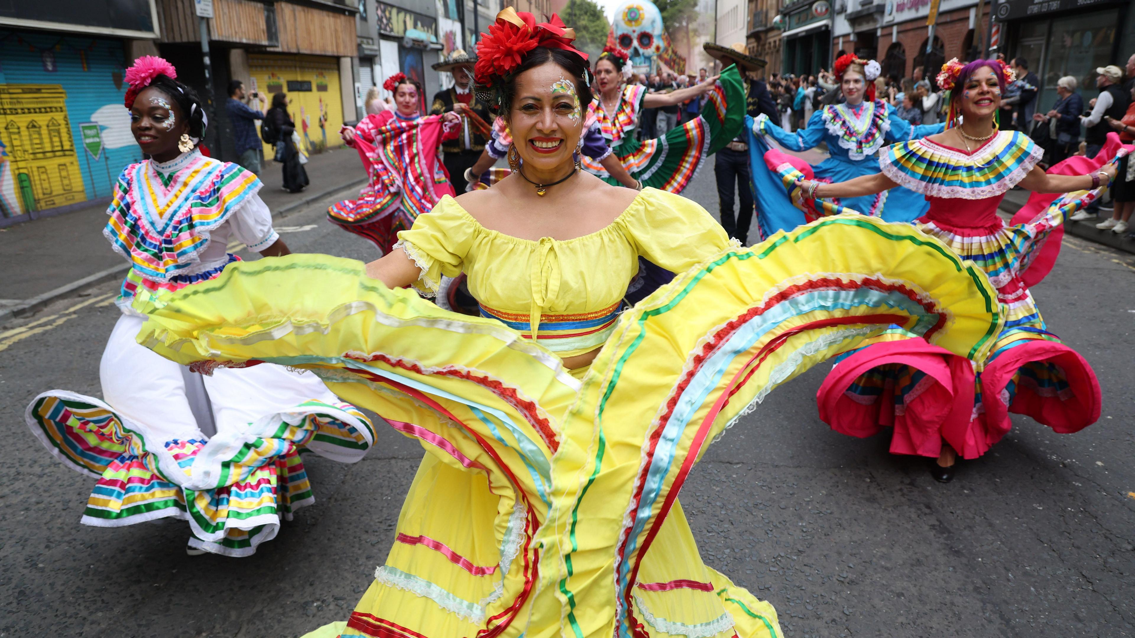 Ladies in traditional dress which is brightly coloured and is flowing as they dance.