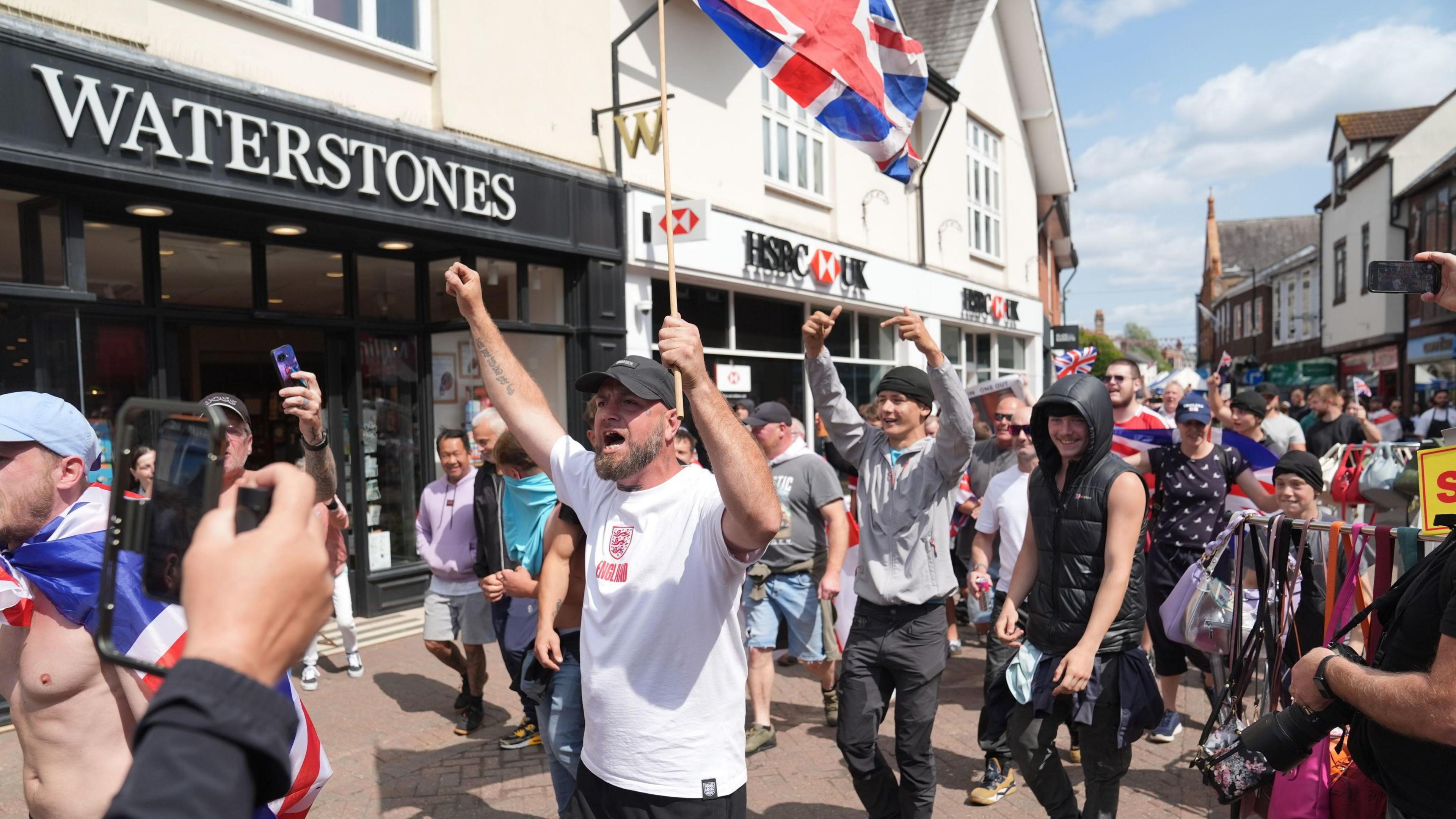 A group of protesters appearing to be chanting while holding a Union Jack