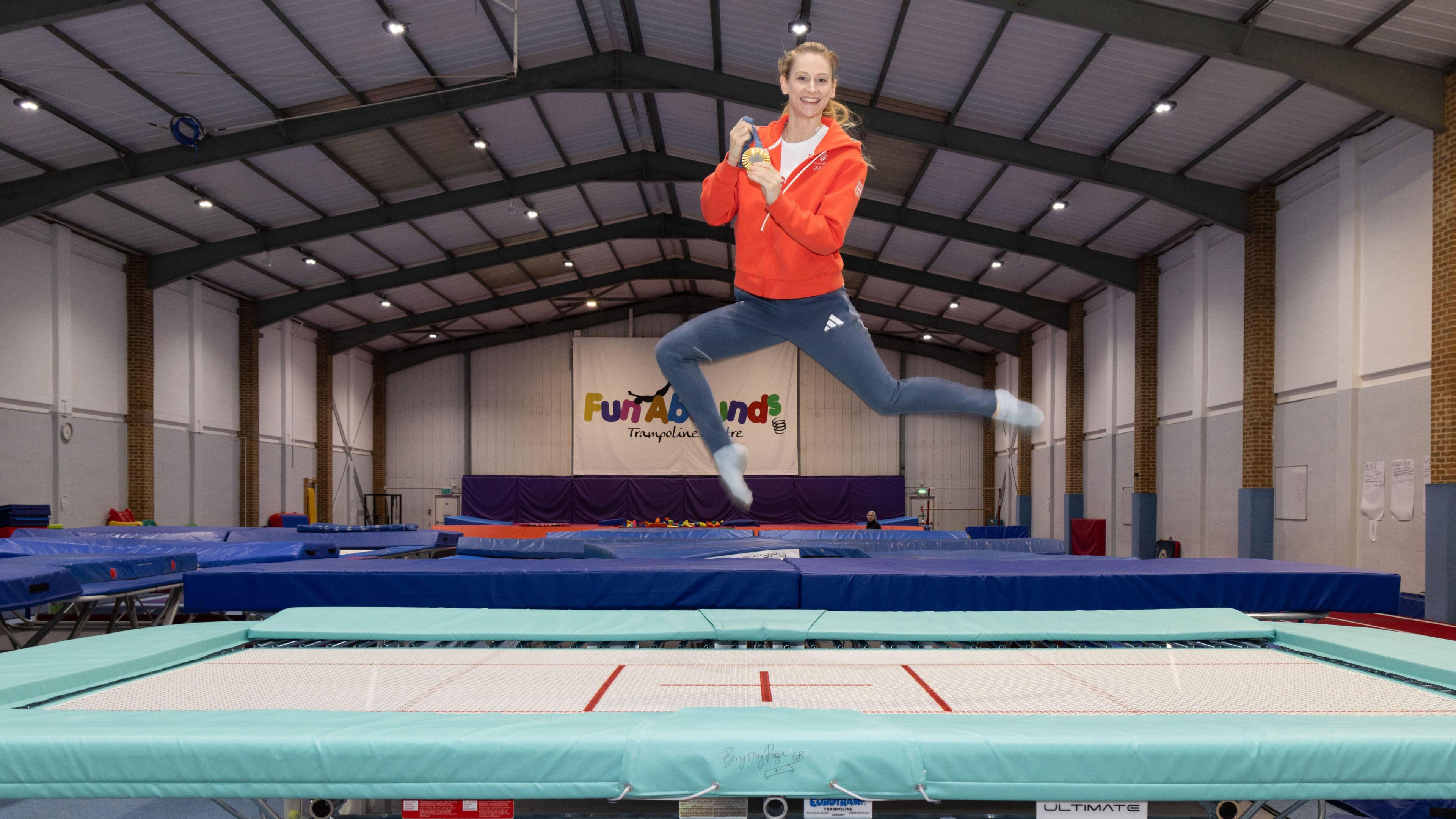 Bryony Page bouncing on a trampoline, smiling, looking into the camera and holding her medal