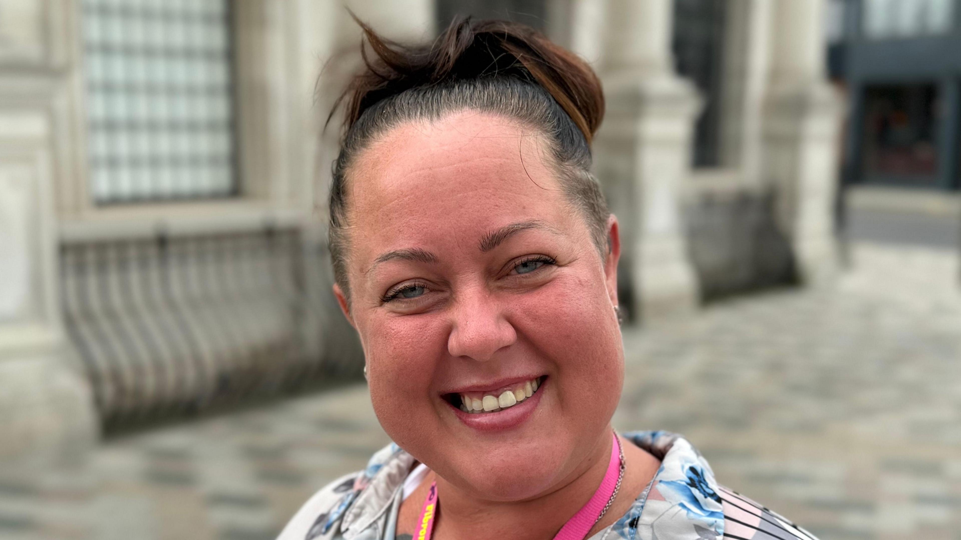 A woman smiling straight at the camera. She is wearing a patterned blouse and a pink lanyard.