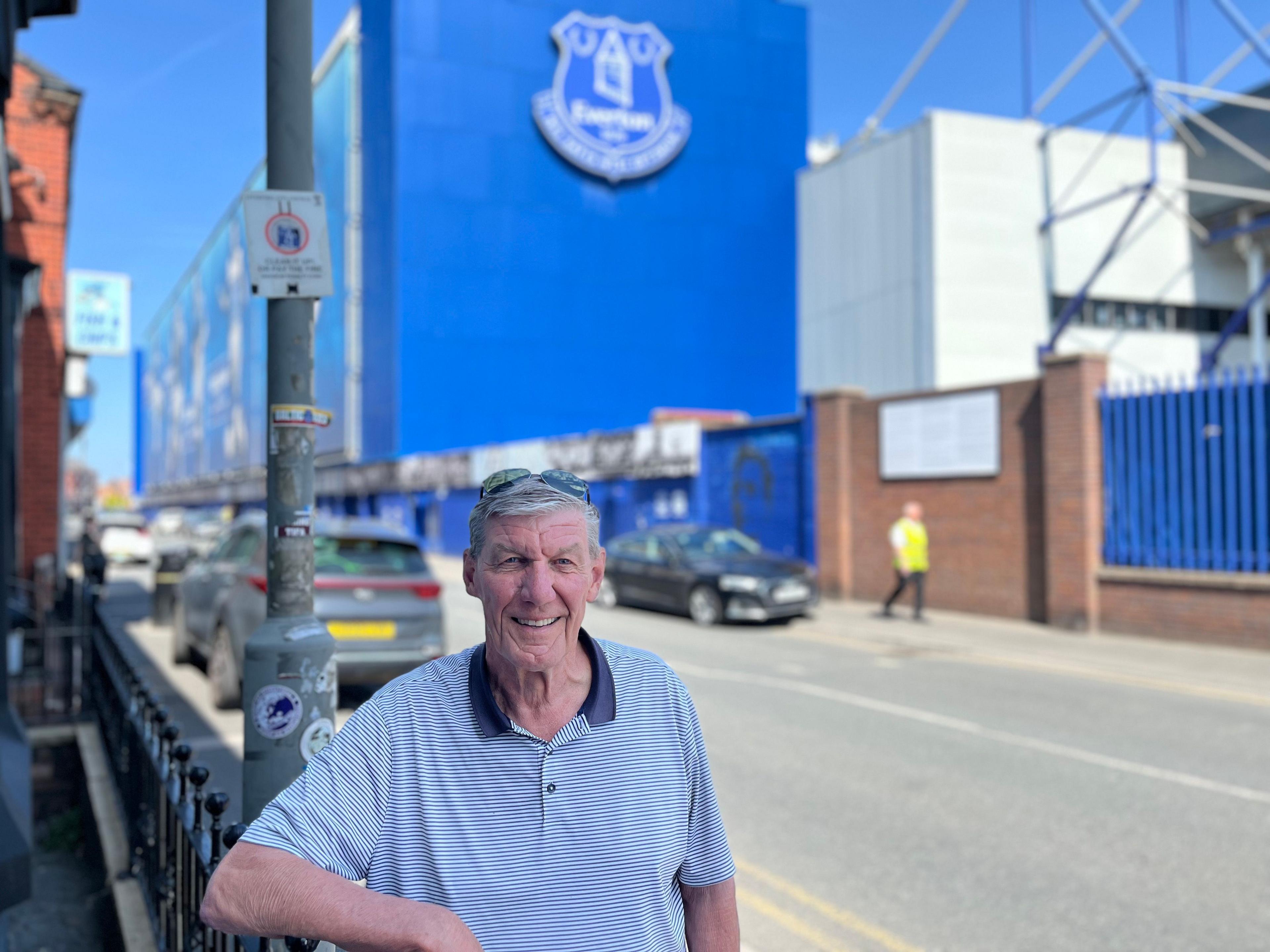 Ray Parr is standing in front of 9 Goodison Road and smiling directly in the camera. Behind him in the background is Goodison Park.
