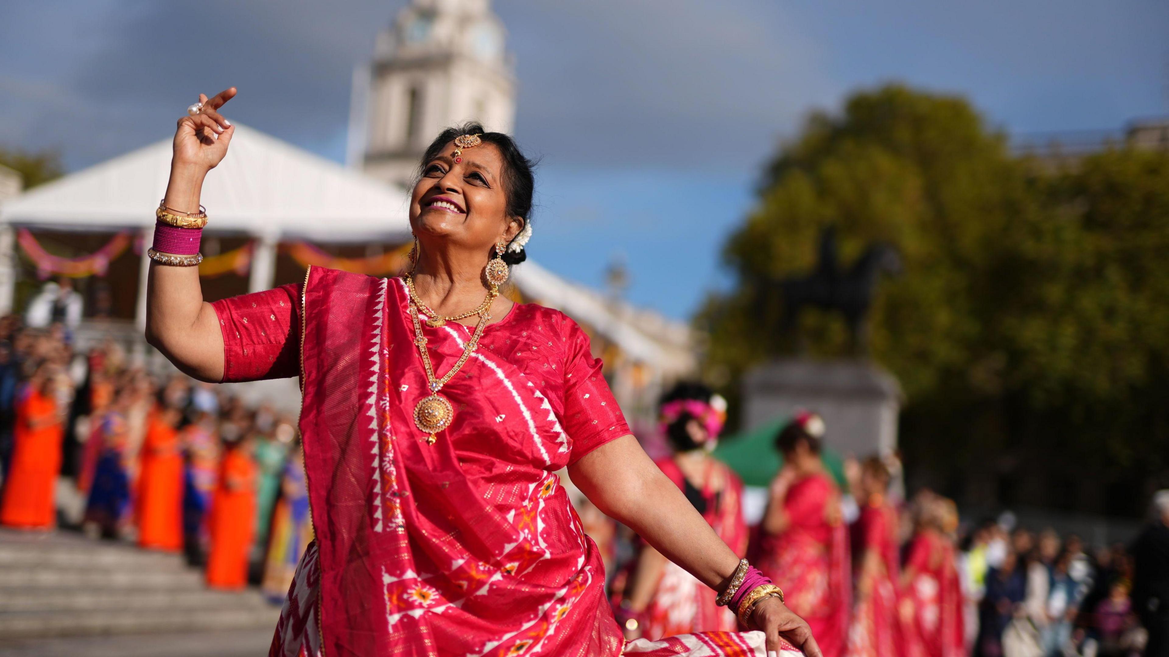 A woman in a pink and white sari looks to the sky while dancing during the event