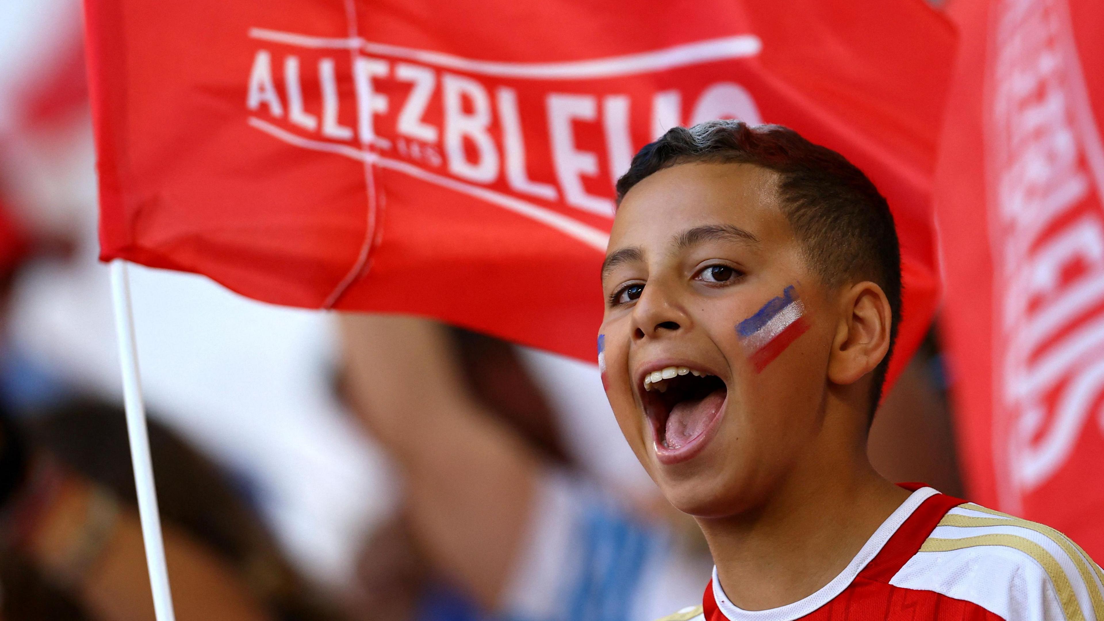 A boy with a painted face cheers while holding a flag