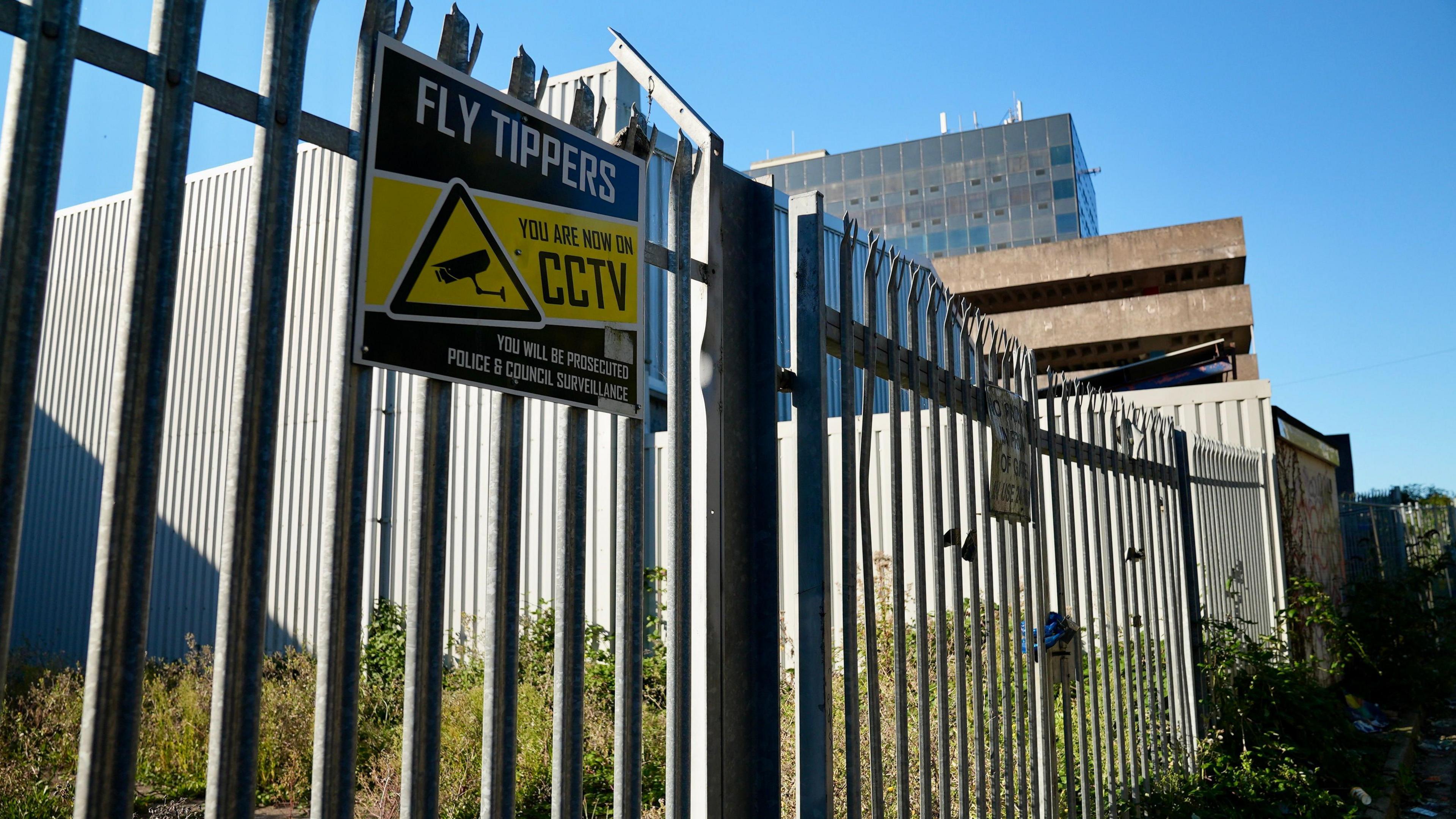 A metal fence with a sign on it saying, "fly-tippers you are now on CCTV".