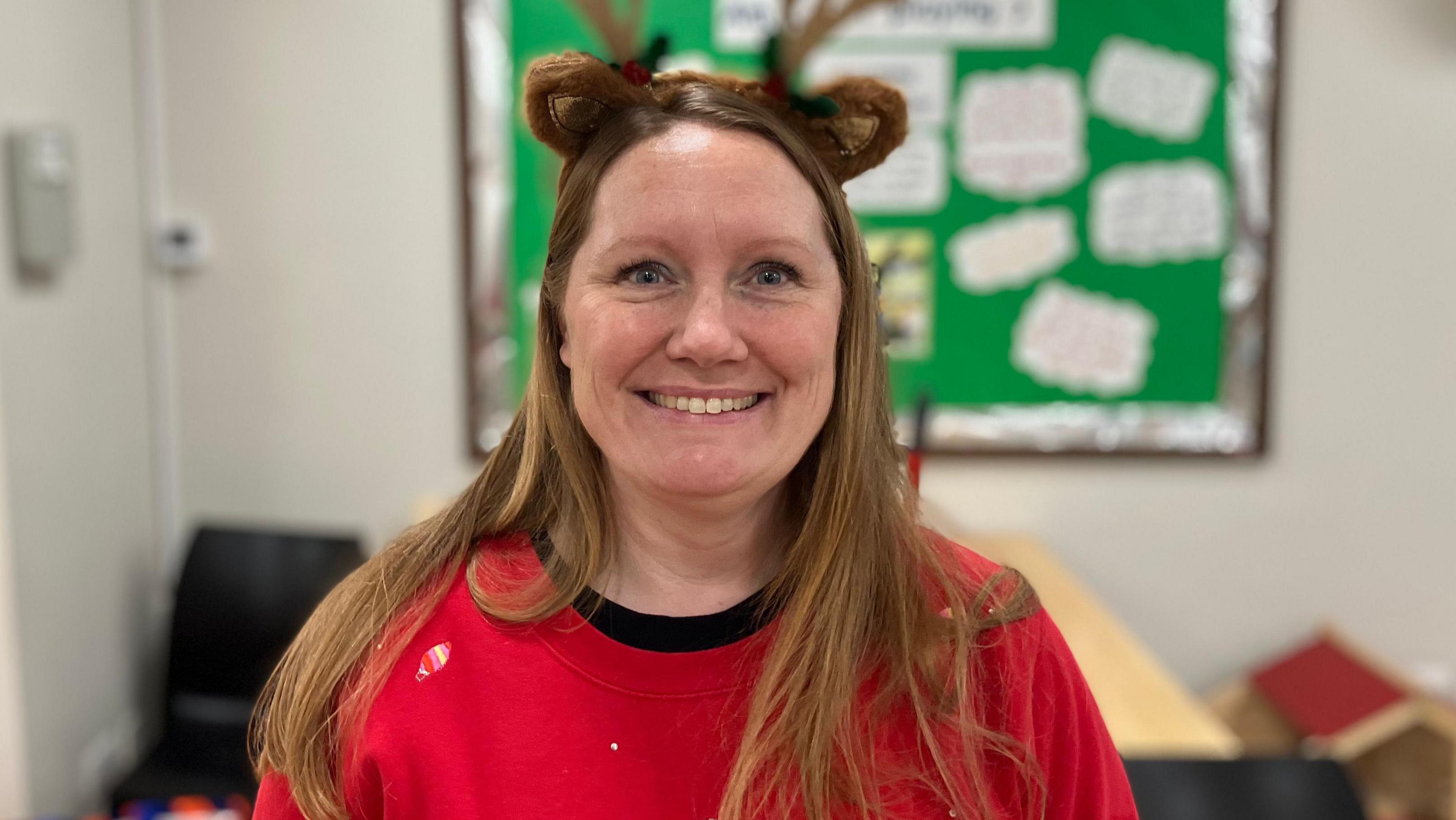 Sophie Townsend in a red jumper looks straight at the camera and smiles. She has a reindeer antler-shaped headband on her head.