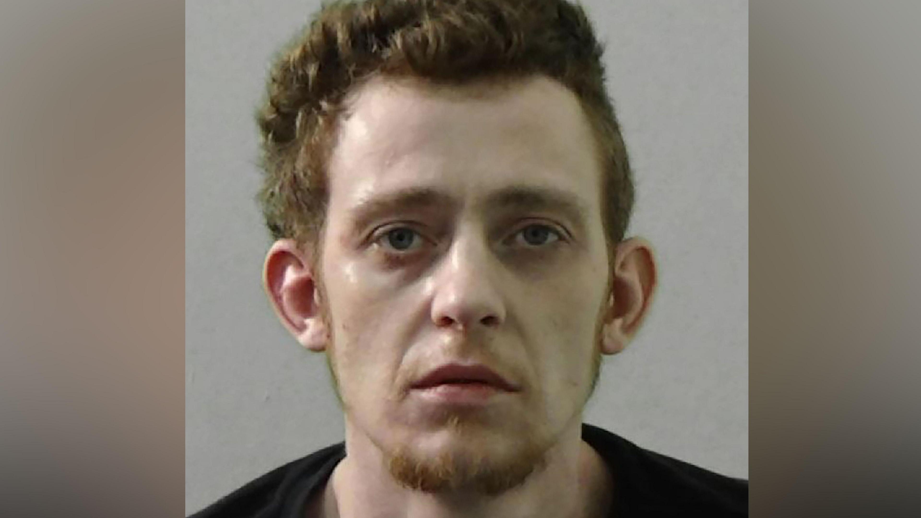 Mugshot of Reece Galbraith. He has thick ginger hair and a ginger goatee and a very pale face. He is wearing a black t shirt
