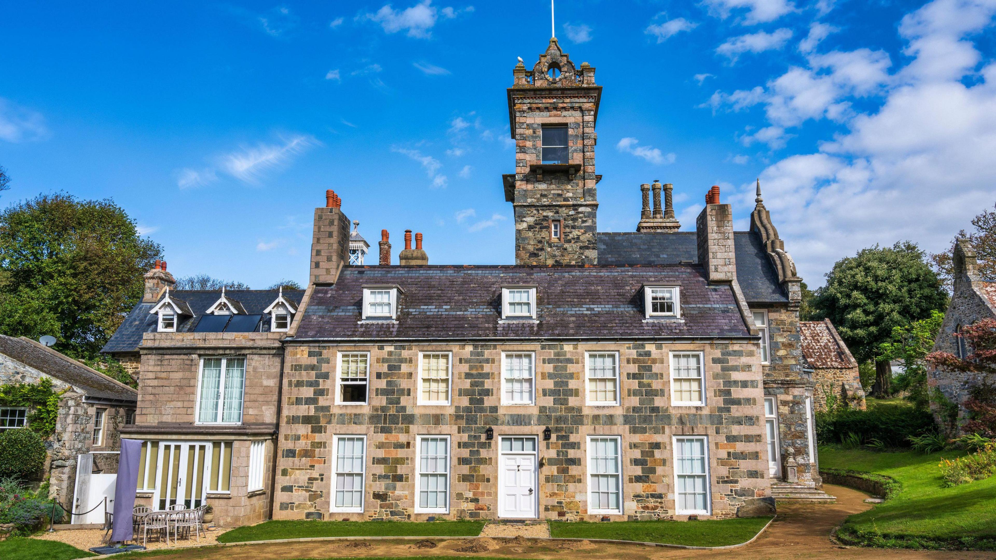 Front facing image of La Seigneurie building, it is a large stately home-esque building with several chimneys and a brick tower emerging from the roof