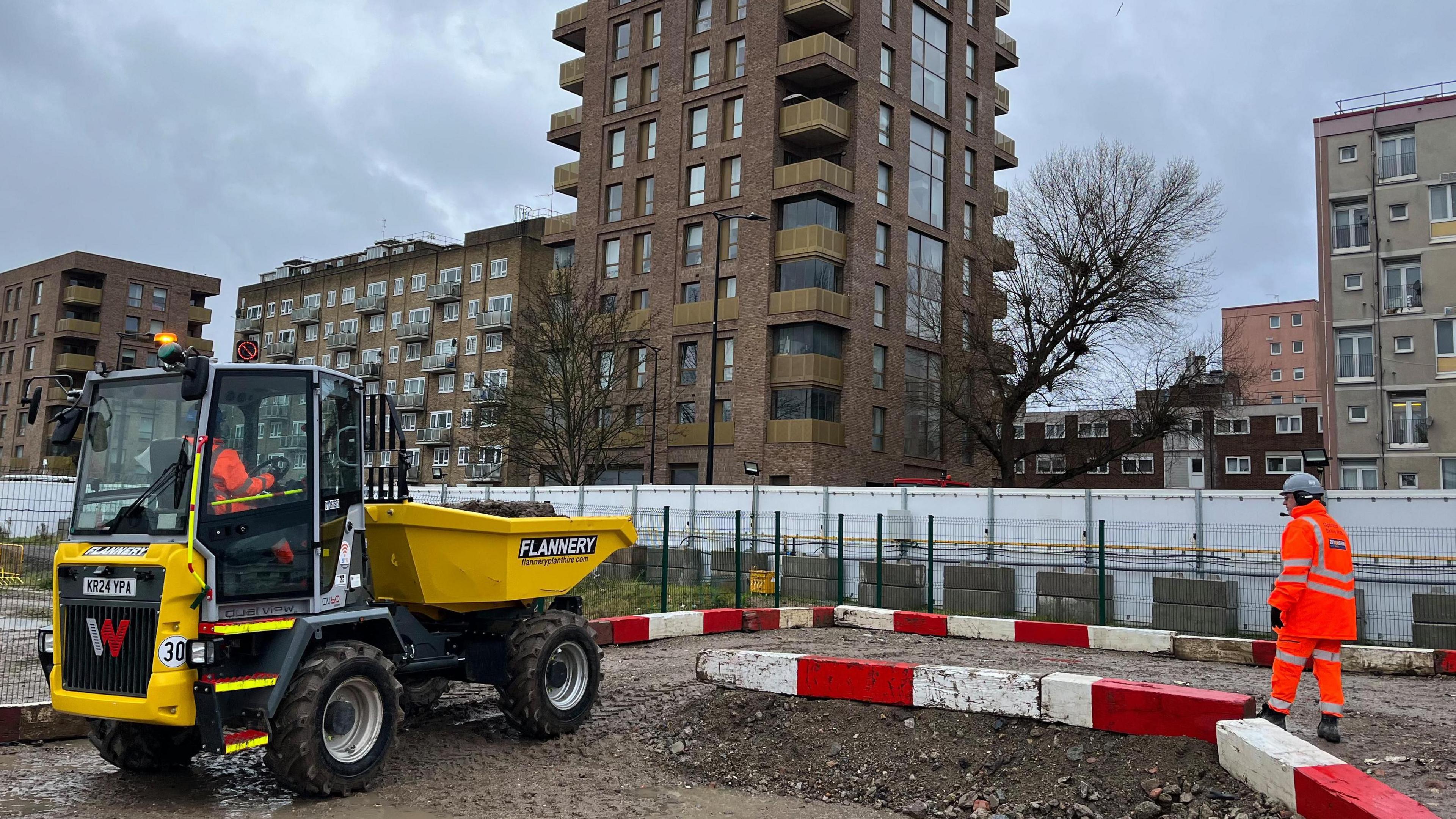 A dumper truck is driving between red and white bollards.