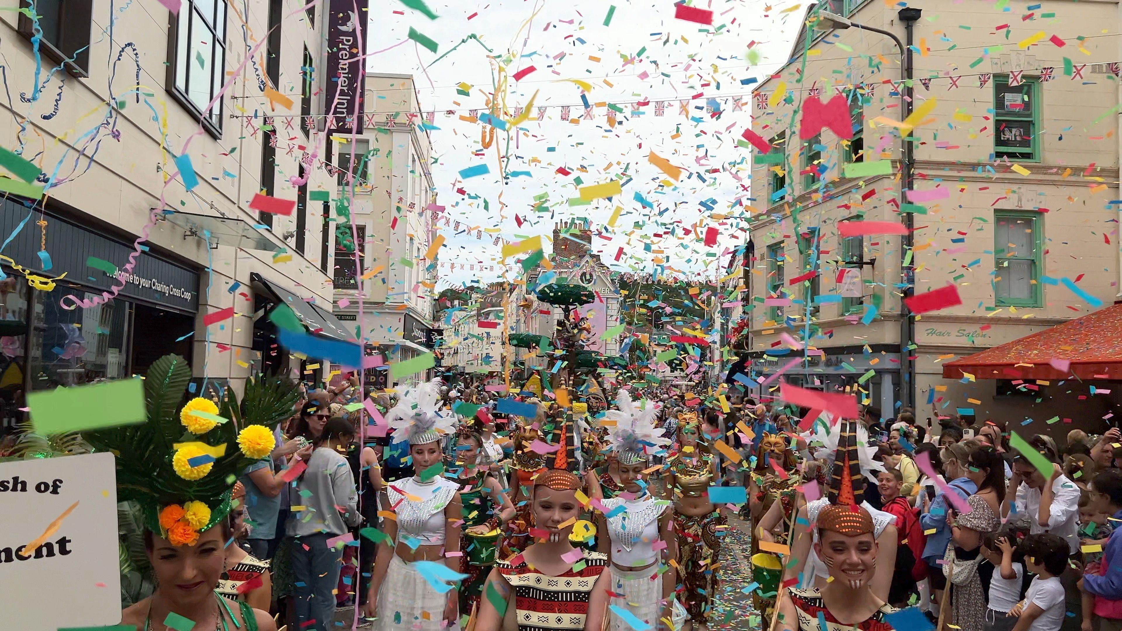 A street in St Helier engulfed by multicoloured confetti and people, some dressed in costume and others spectators of the Battle of Flowers.