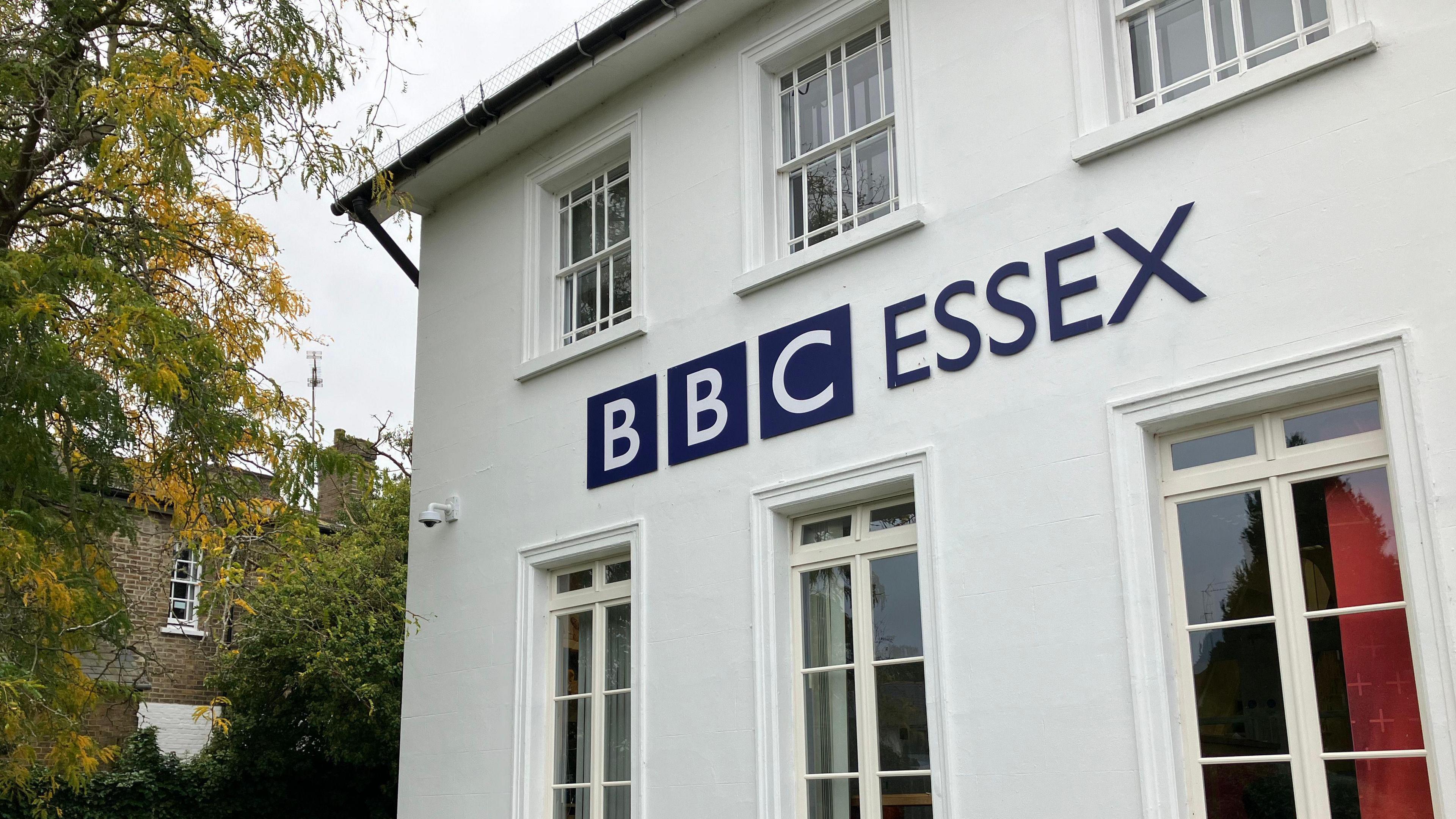 The BBC Essex base, which is a two-storey, white building with the lettering "BBC Essex". It has windows and to the left is a tree.