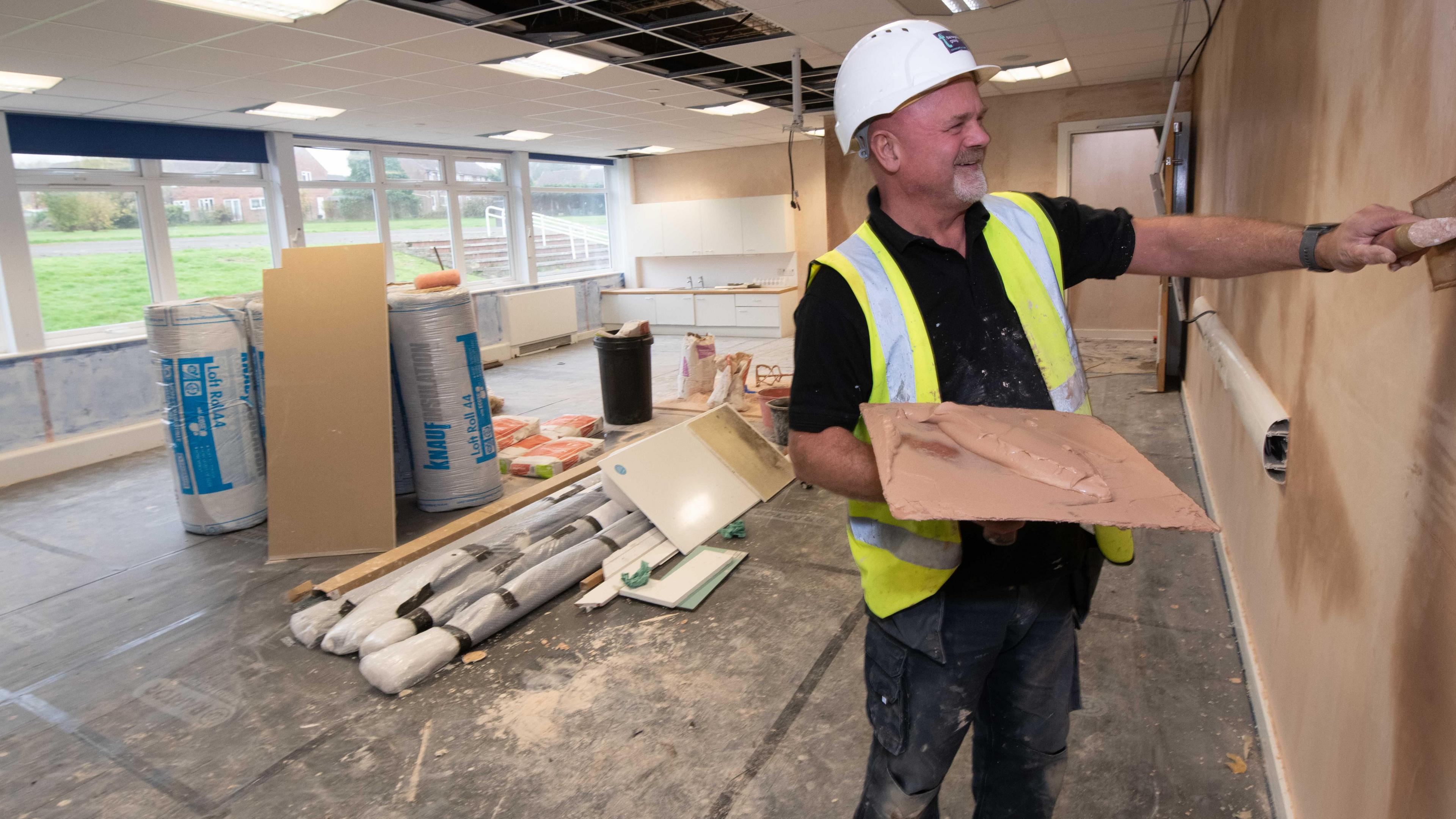 A man in a hard hat and hi-vis jacket plastering a wall 