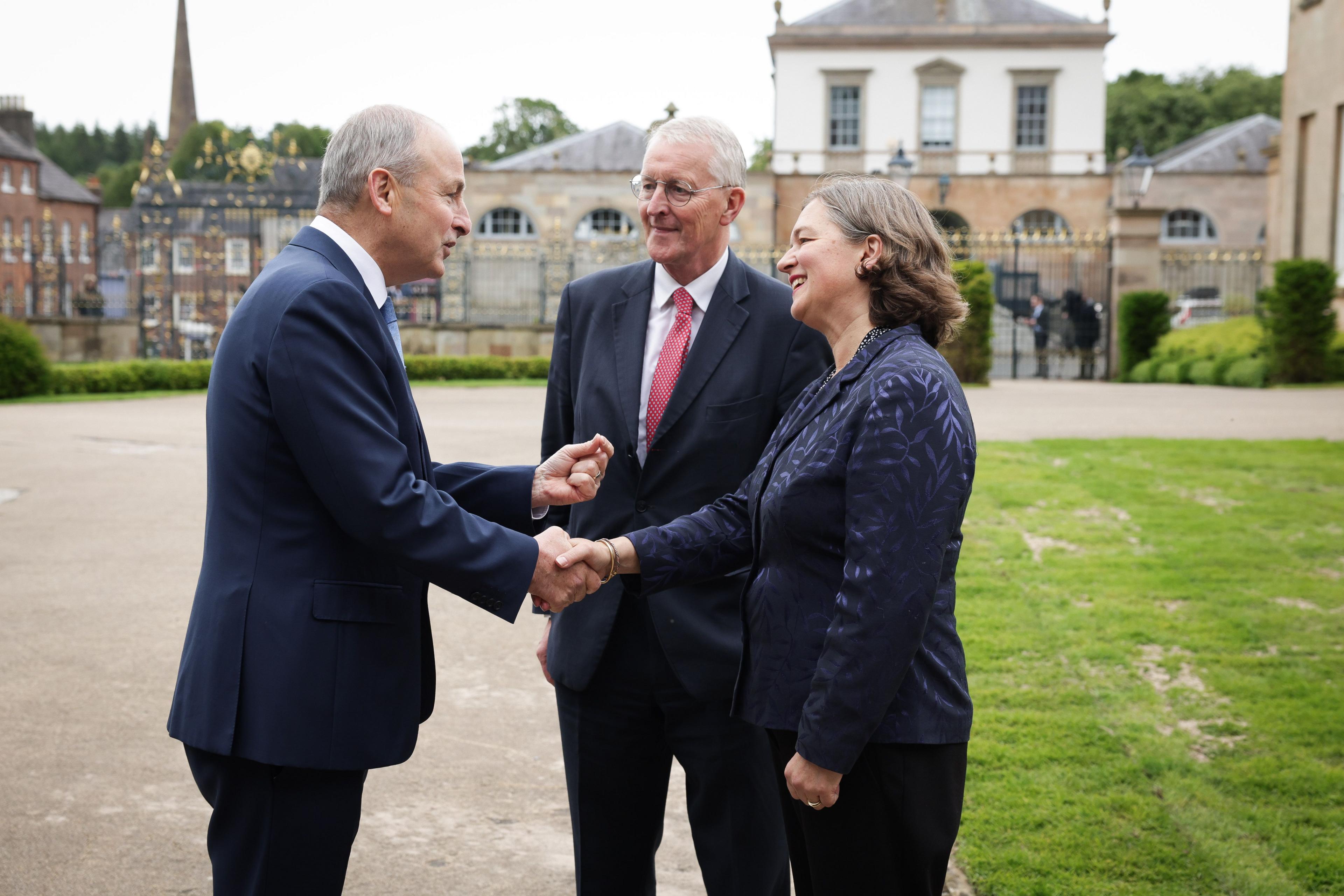 Michael Martin shaking hands with Fleur Anderson with Hilary Benn and Hillsborough Castle in the background